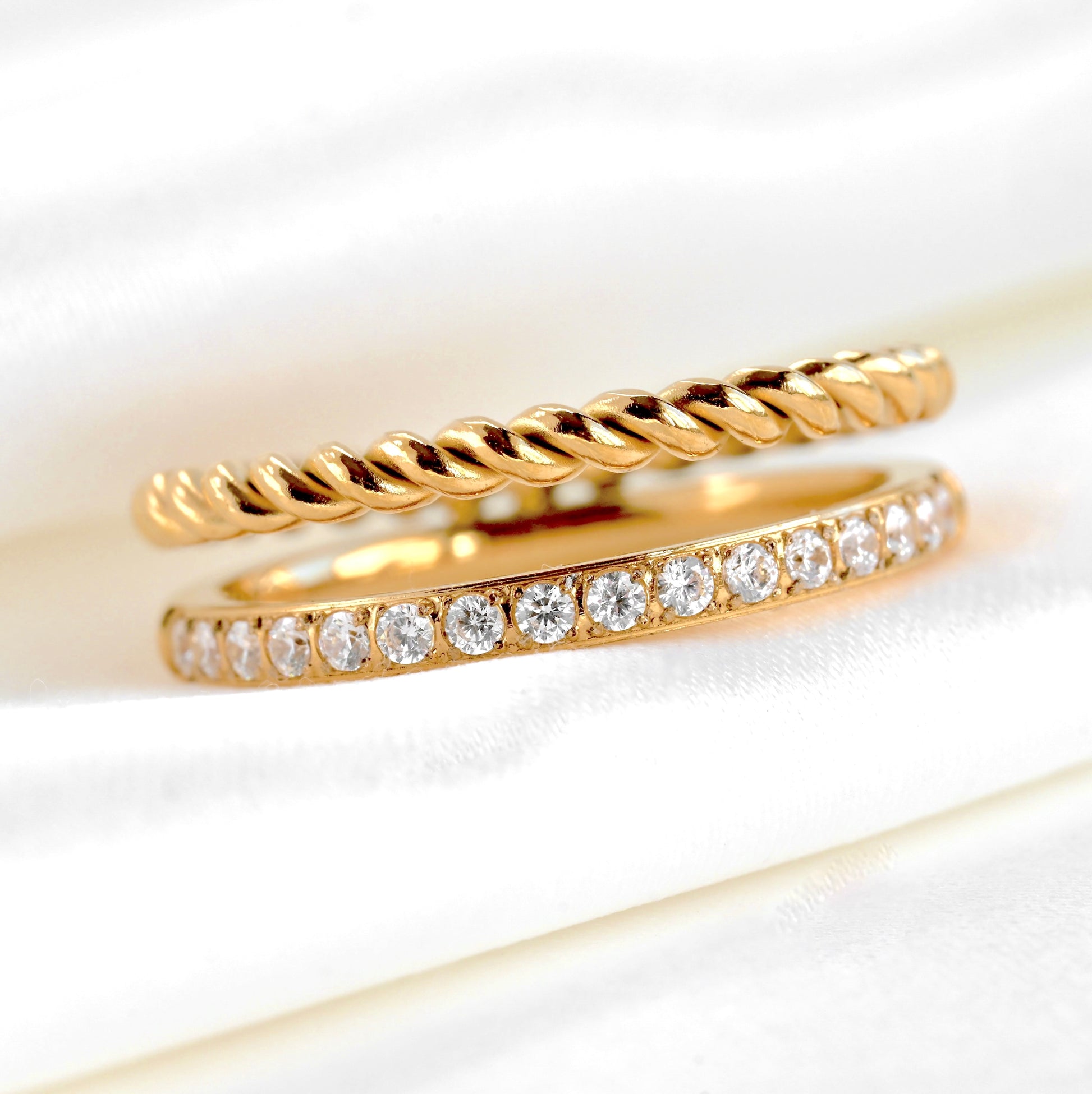 Linked two gold rings with twisted band CZ accents on a white background