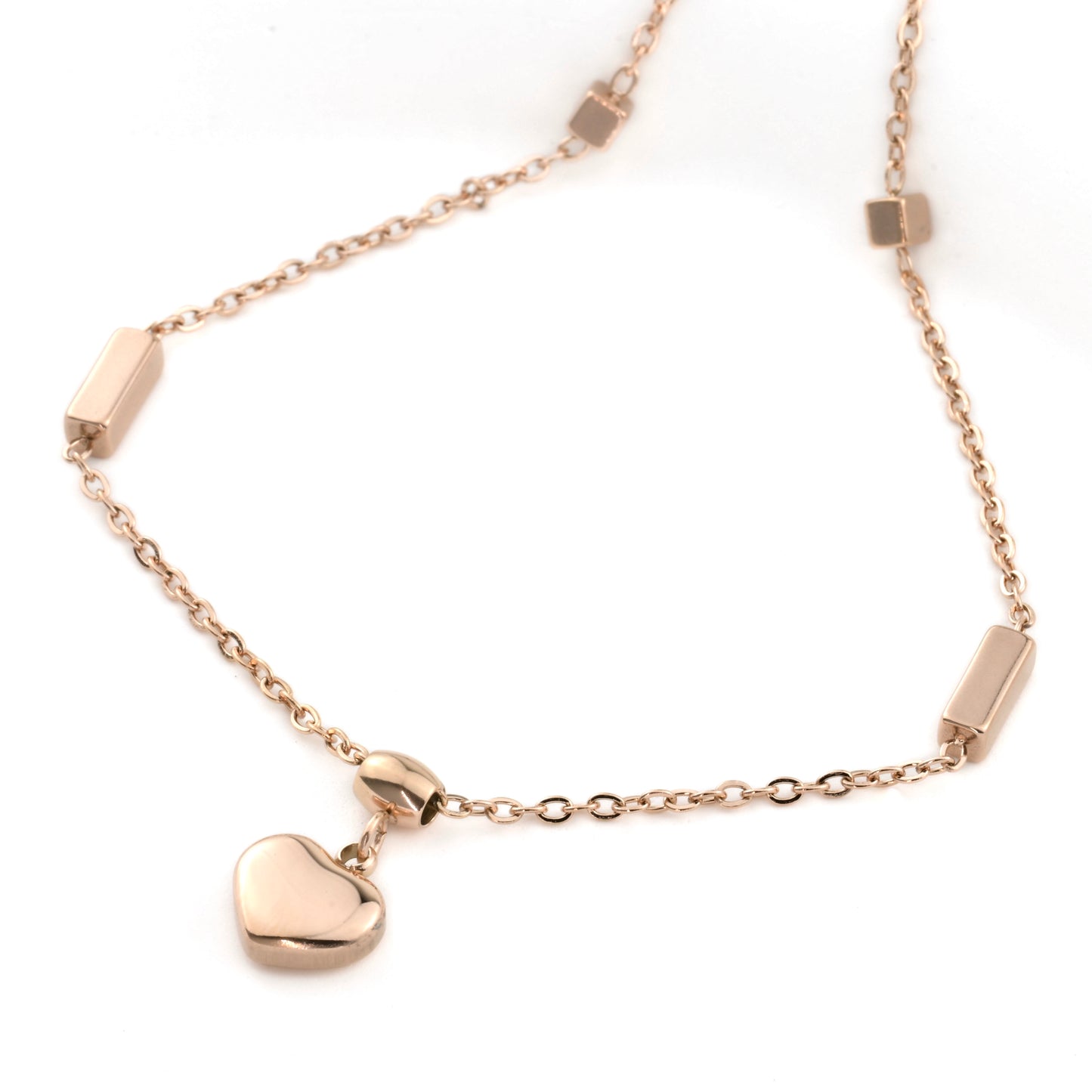 Rose gold heart charm ankle bracelet with geometric beads on a white background
