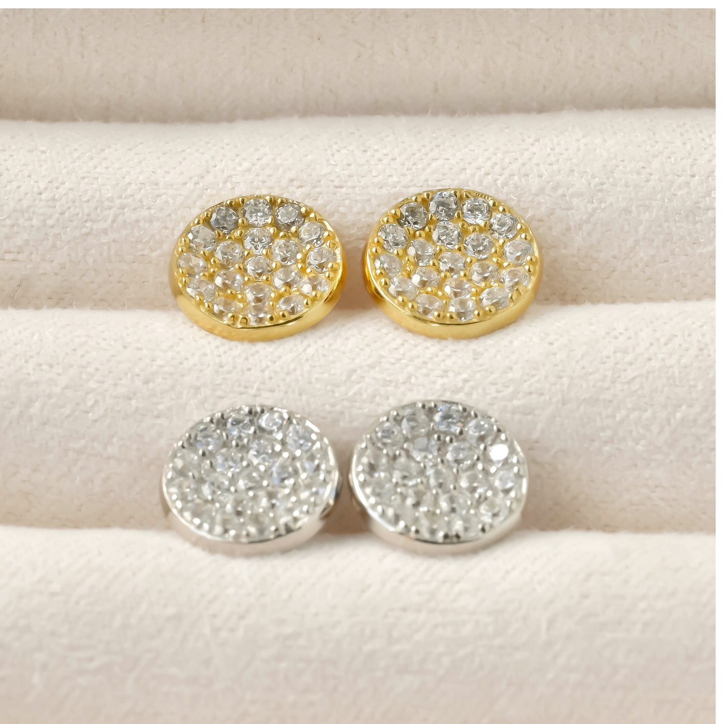 Gold and silver round stud earrings with gemstones on a beige surface