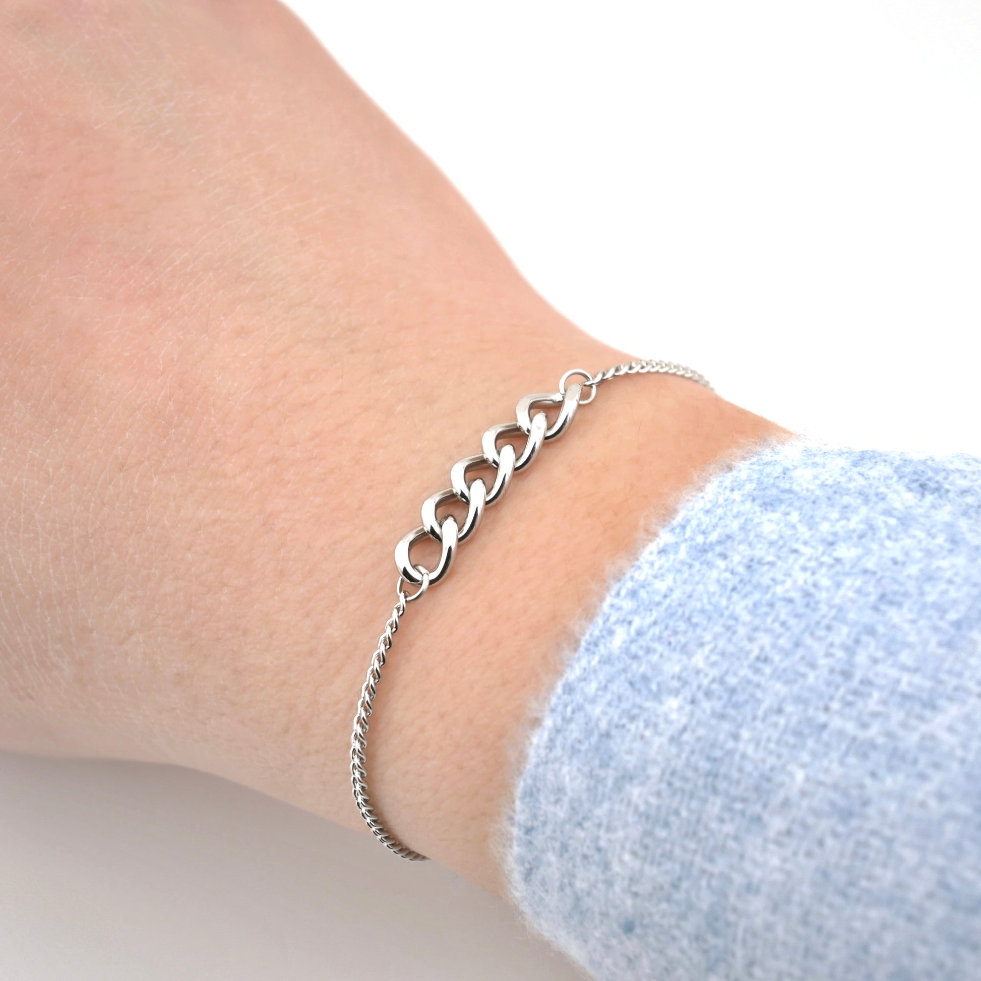 Silver link chain bracelet on a wrist with a light blue sleeve against a white background