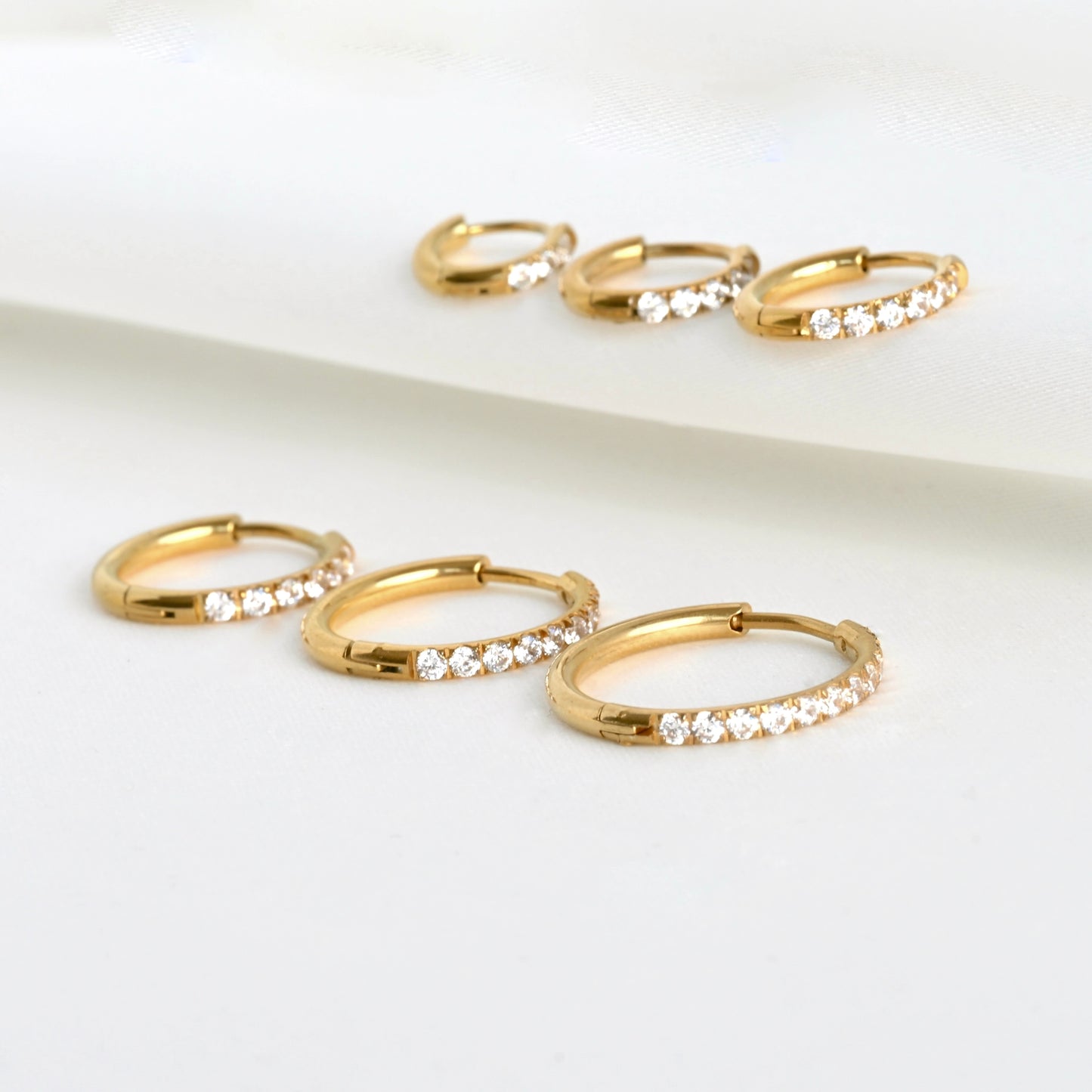 Gold simulated diamond hoop earrings with embedded crystals on a light background