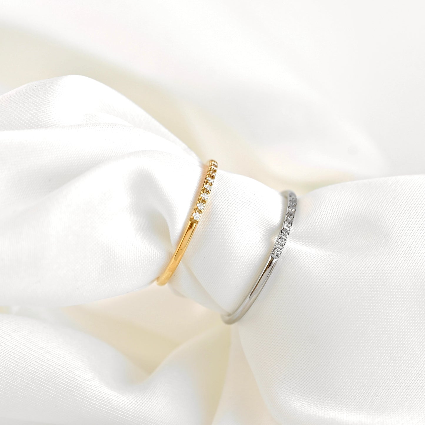 Side view of two dainty gold and silver diamond rings on a white fabric background.