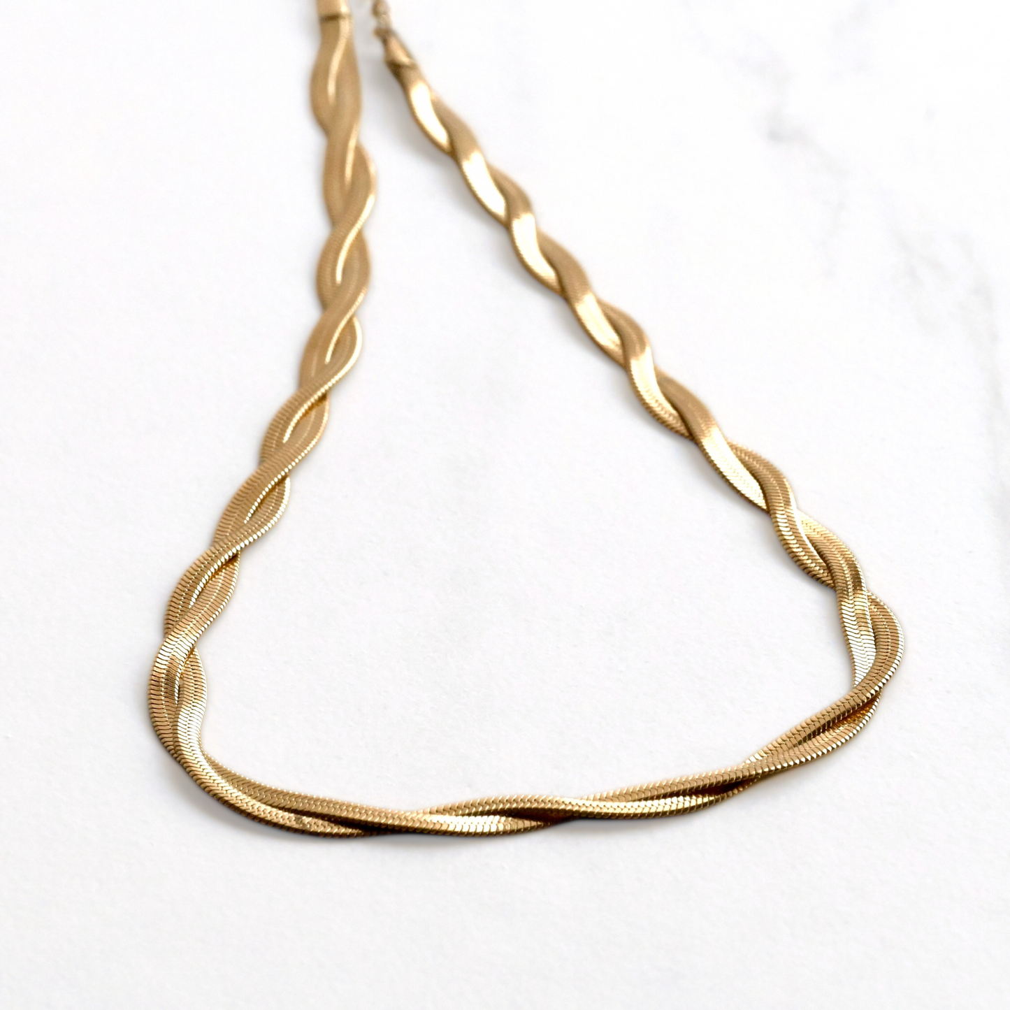 Close up view of gold twisted snake chain necklace on a white marble background