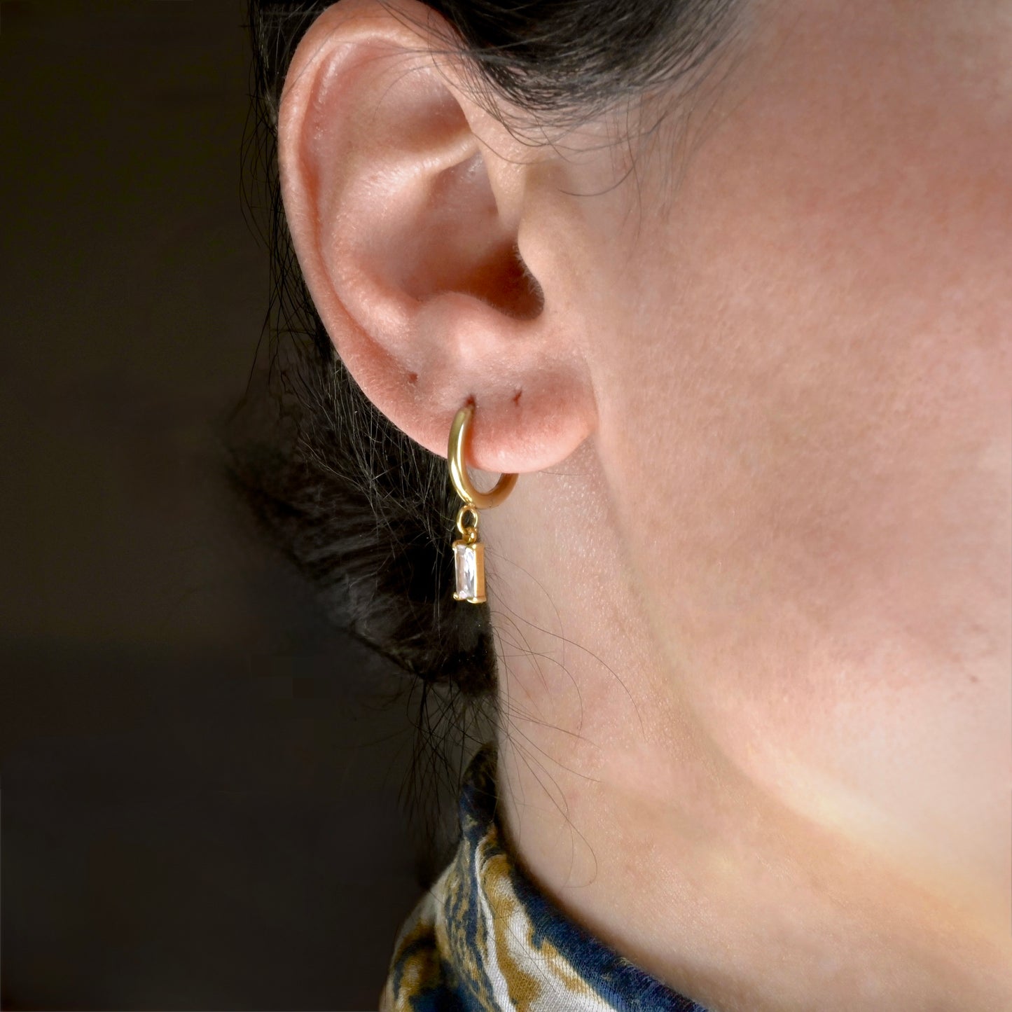 Close-up of an ear wearing a gold hoop earring with a dark background