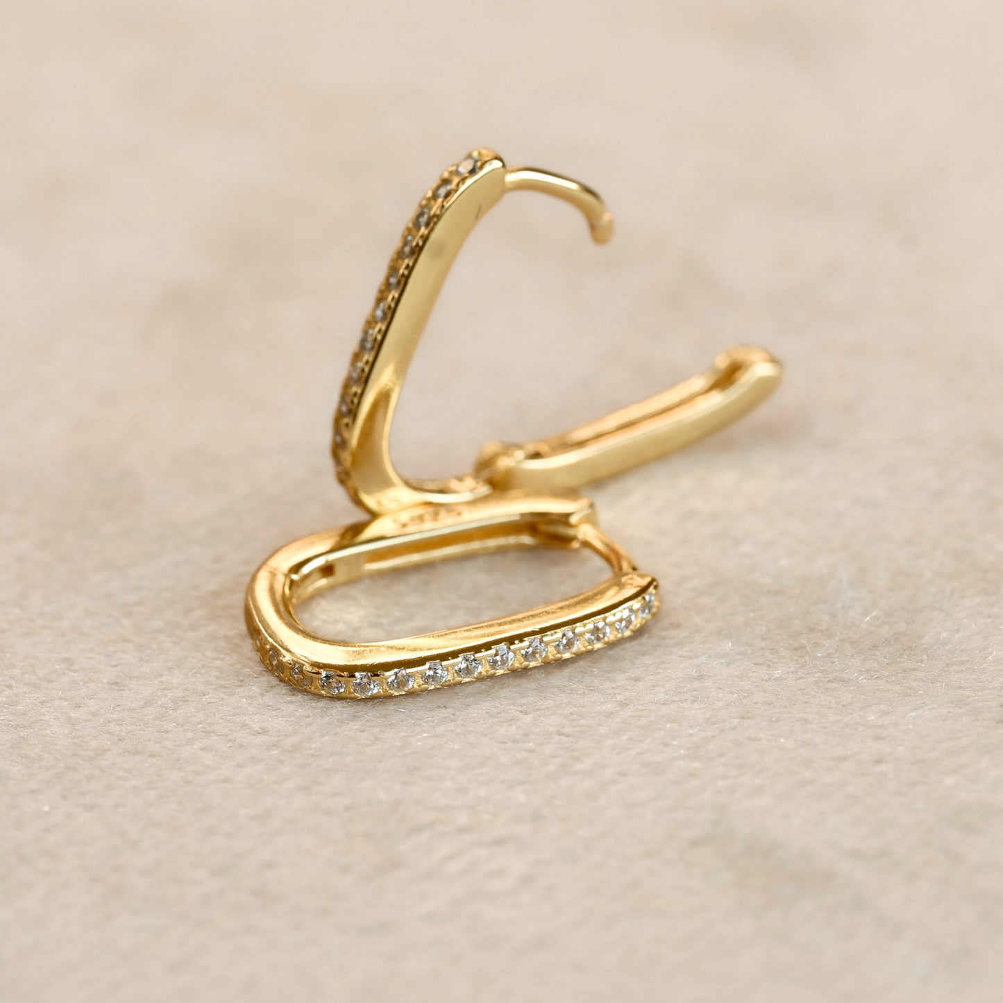 Gold pave U-shaped hoop earrings , one closed and flat on beige surface, other upright and open showing clicker closure.
