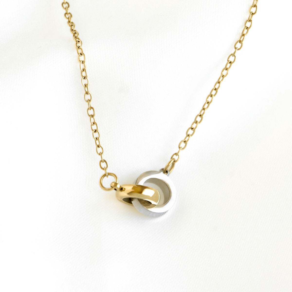 A gold chain necklace with a pendant featuring interlocking gold and silver rings, displayed on a clean white background.