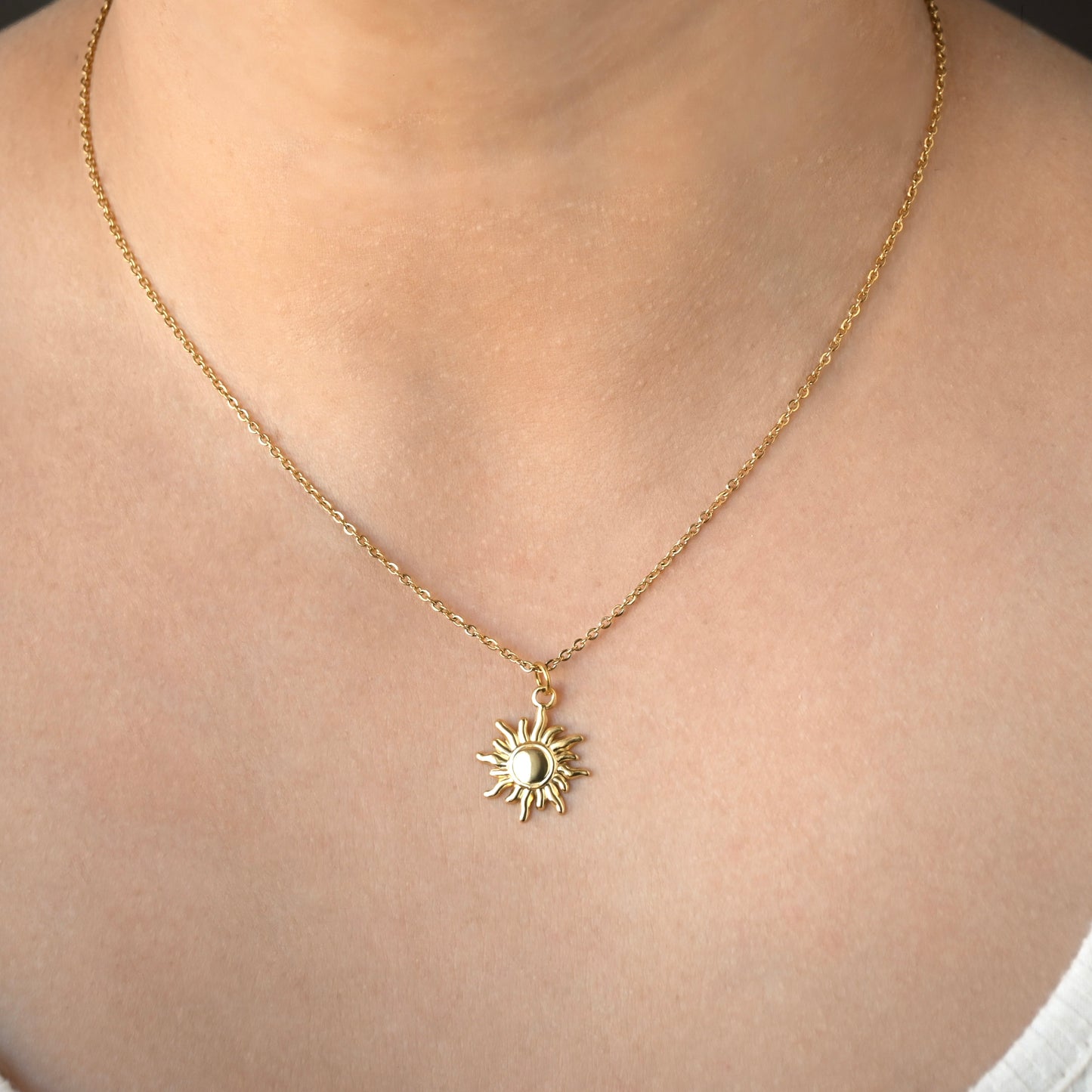 Gold necklace with a classic sun pendant on a person's neck