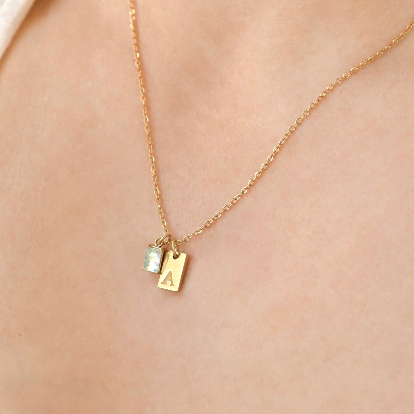 Dainty Gold pendant with a small letter charm and october birtstone "opal" on a person's neck