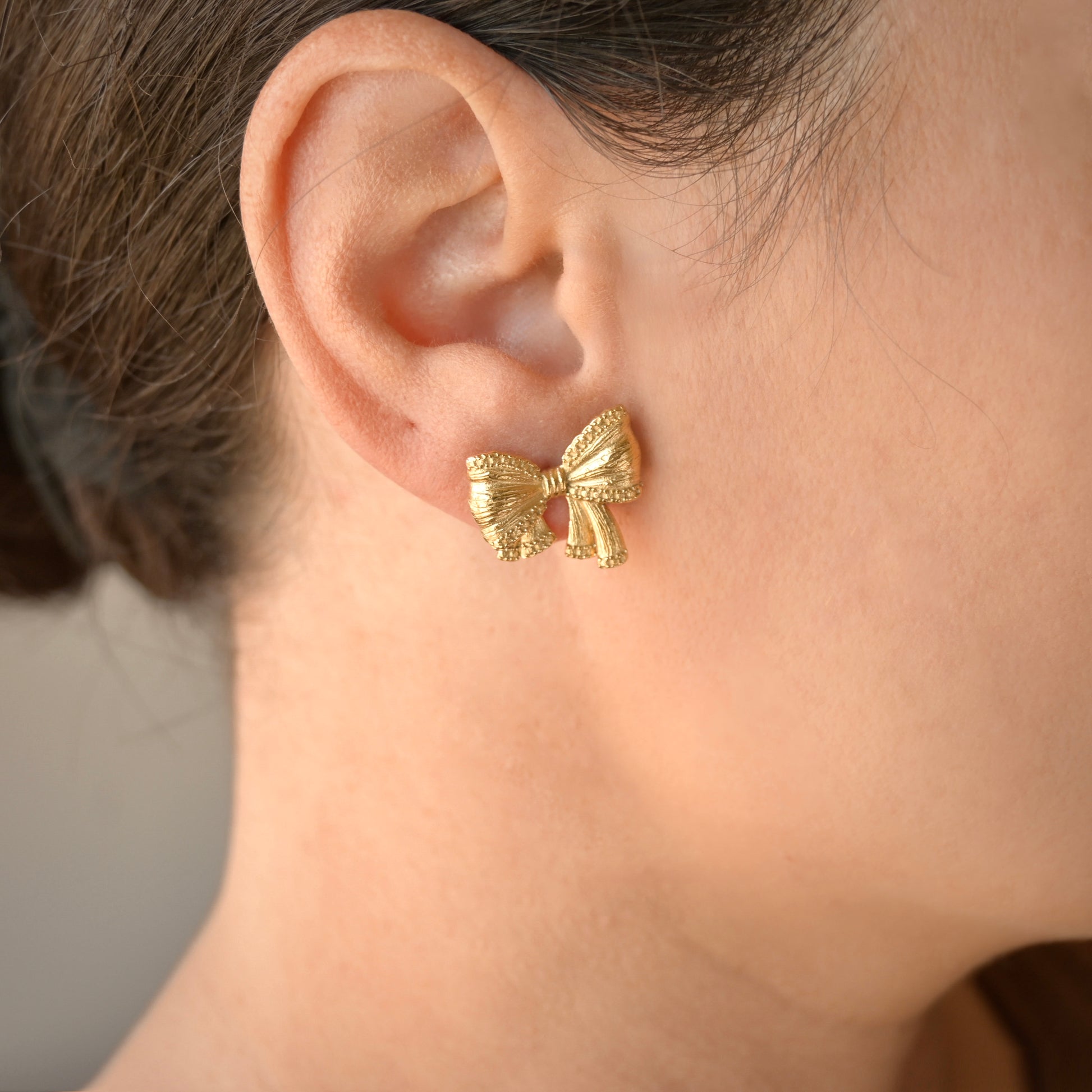Textured gold bow earring worn on a person's ear with a neutral background