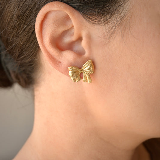 Textured gold bow earring worn on a person's ear with a neutral background