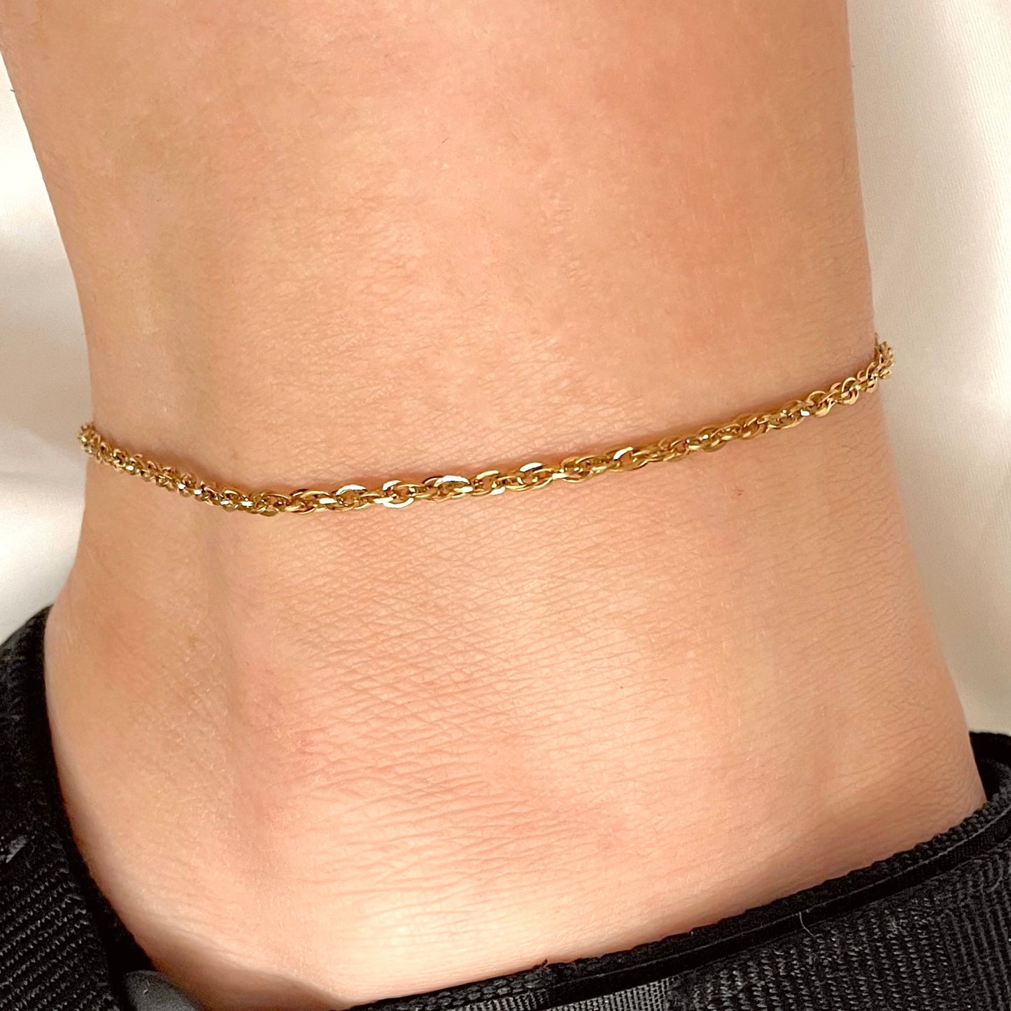 Gold rope chain anklet on a person's ankle against a neutral background