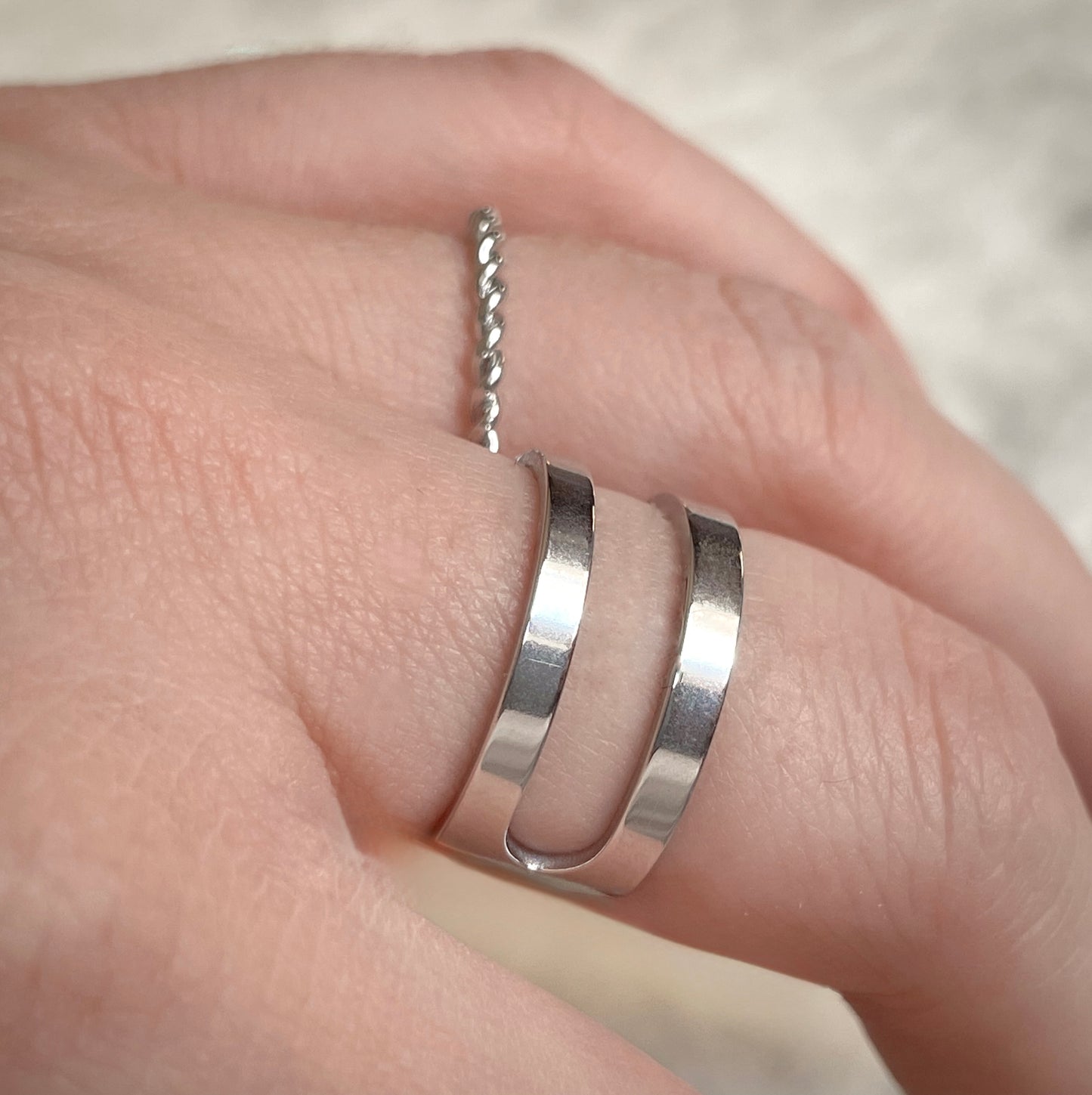 Side view of layered silver ring stacked with a dainty twisted band with a plain background