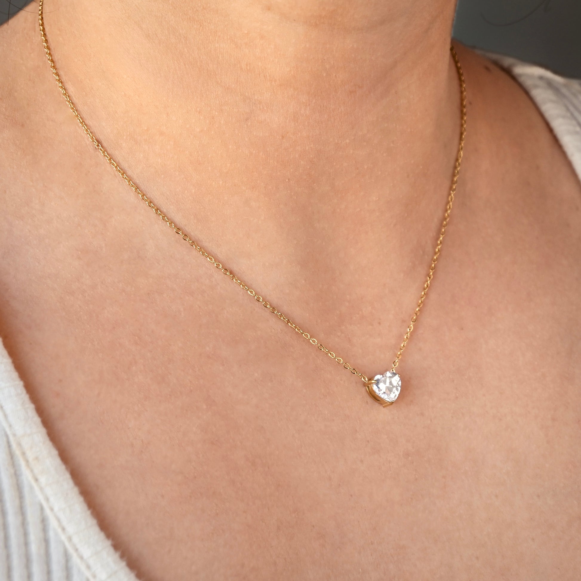 gold heart solitaire pendant on a person's neck wearing a beige top