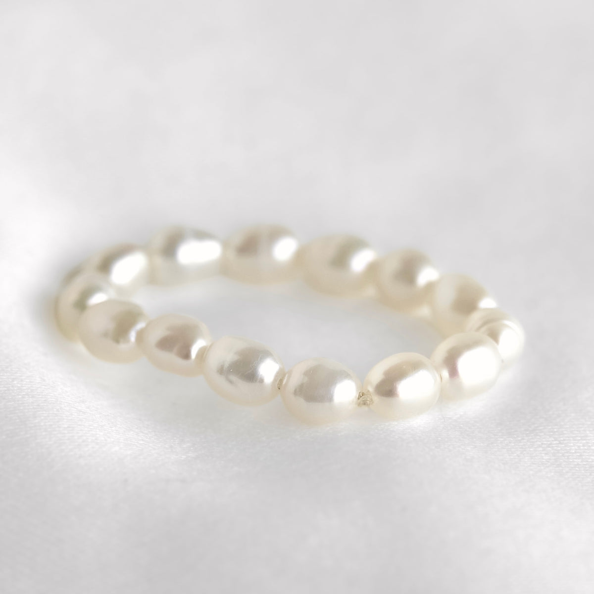 A beaded stretch ring made of irregular white freshwater pearls, photographed on a soft white fabric background.