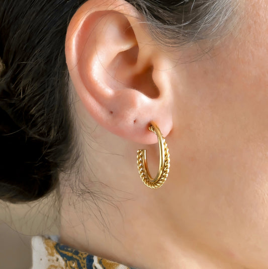 Close-up of an ear wearing a entwined gold C hoop earrings with a blurred background