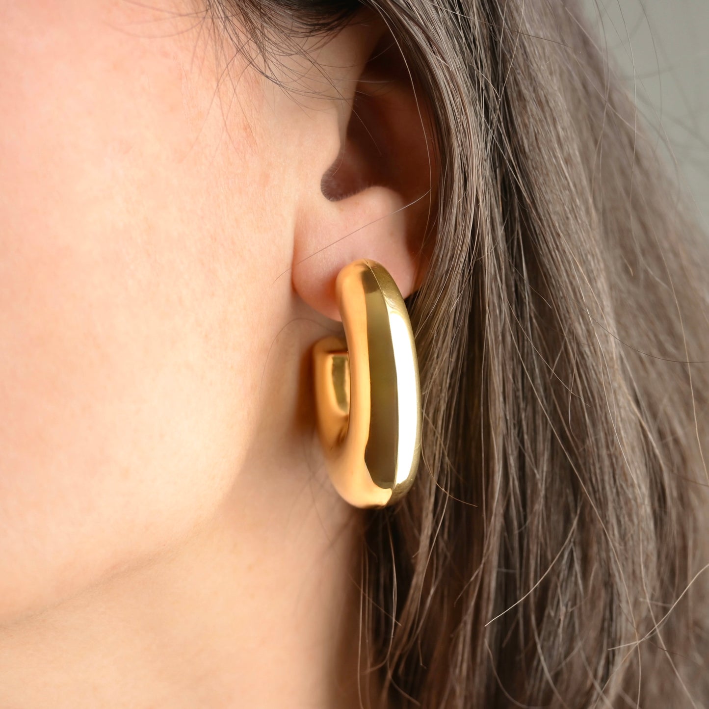 Large Chunky Gold earring worn by a person with brown hair.