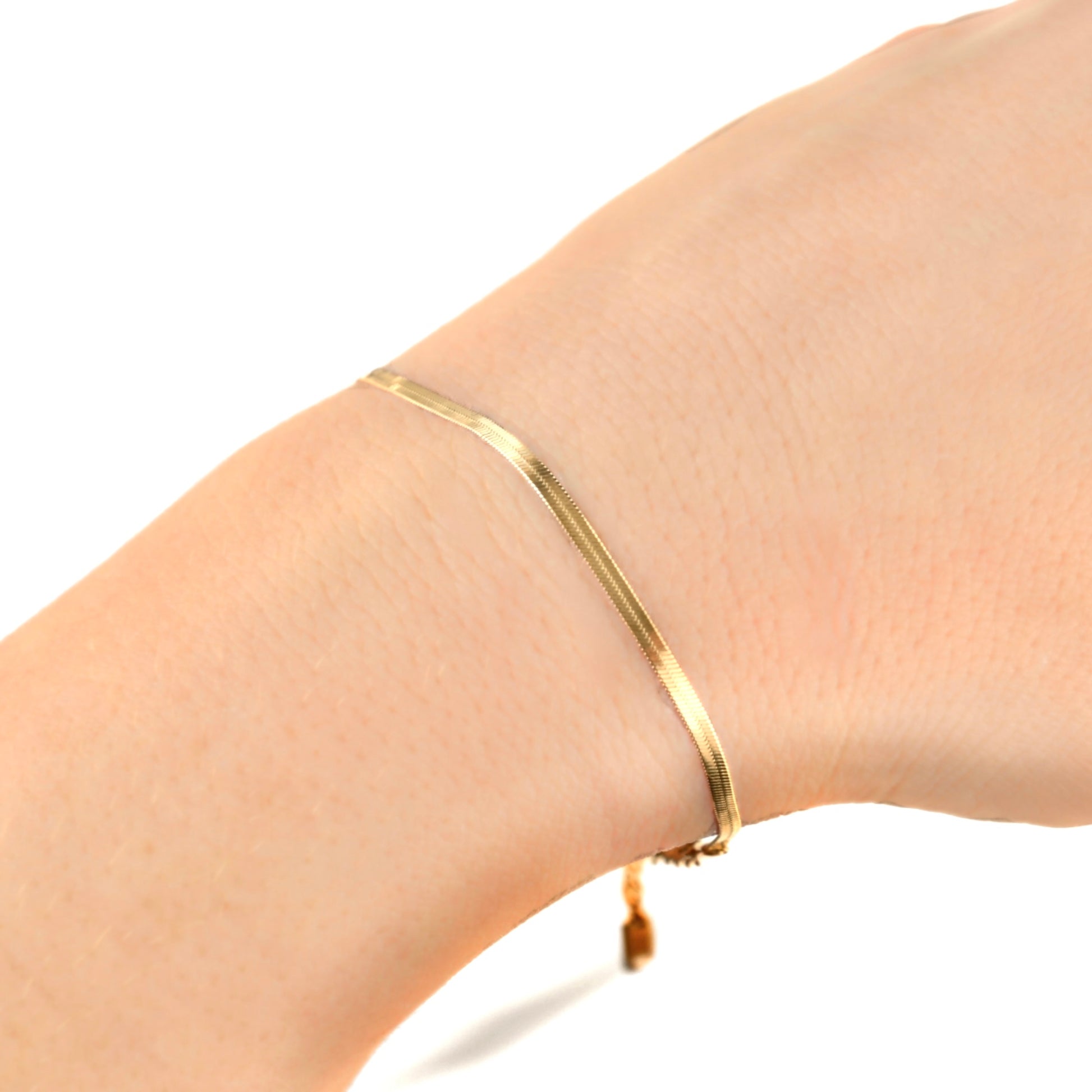 Dainty thin herringbone bracelet in gold on a wrist against a white background