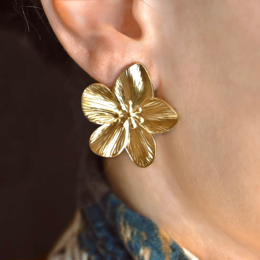Oversized Gold flower earring with intricate details worn on an ear with a blurred background