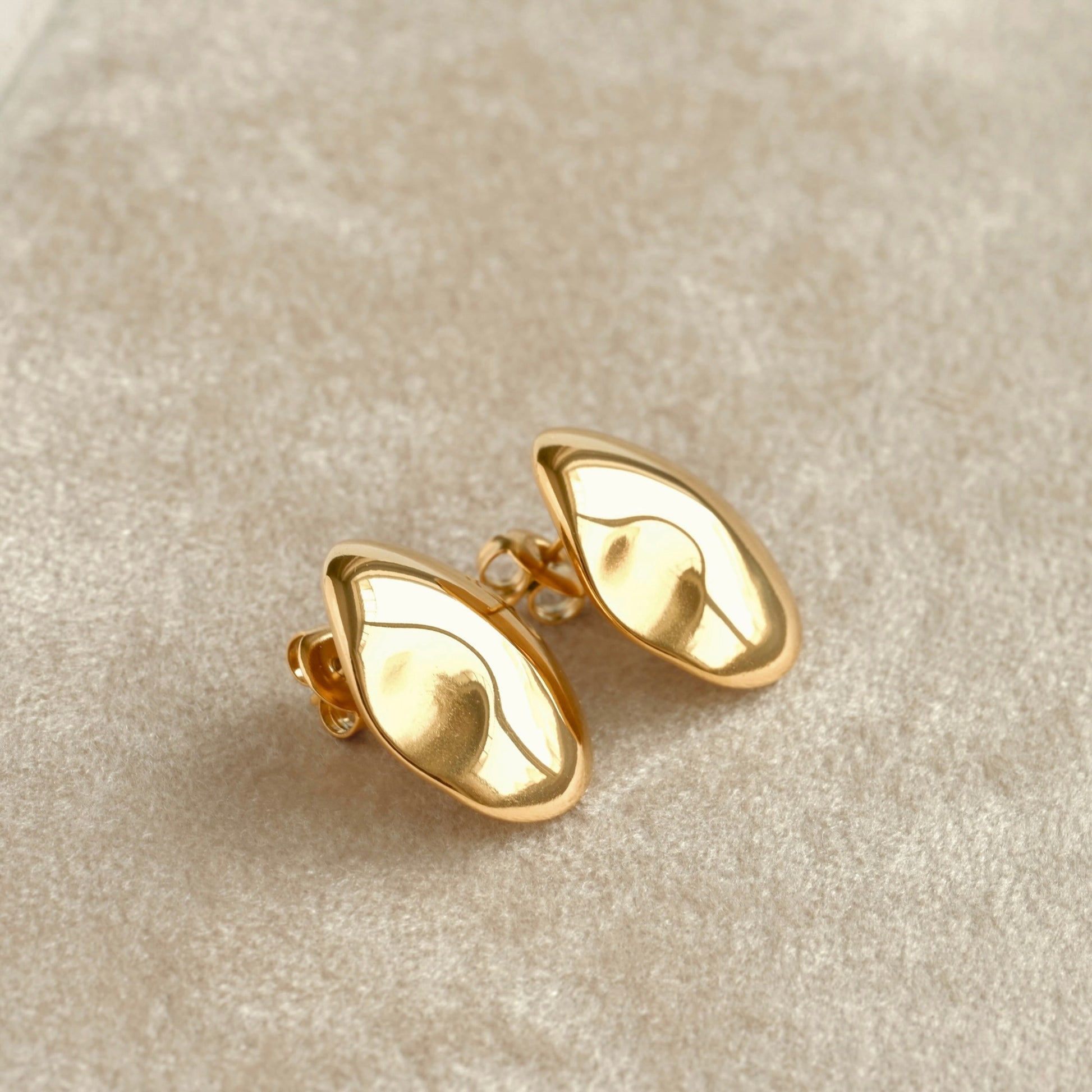 Irregular gold earrings with butterfly backs on a beige fabric background