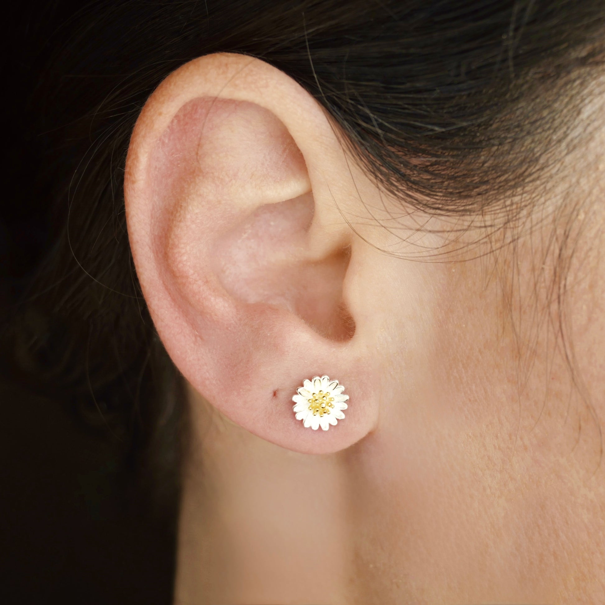 side Close-up view of an ear wearing a medium sized floral earring with a blurred background