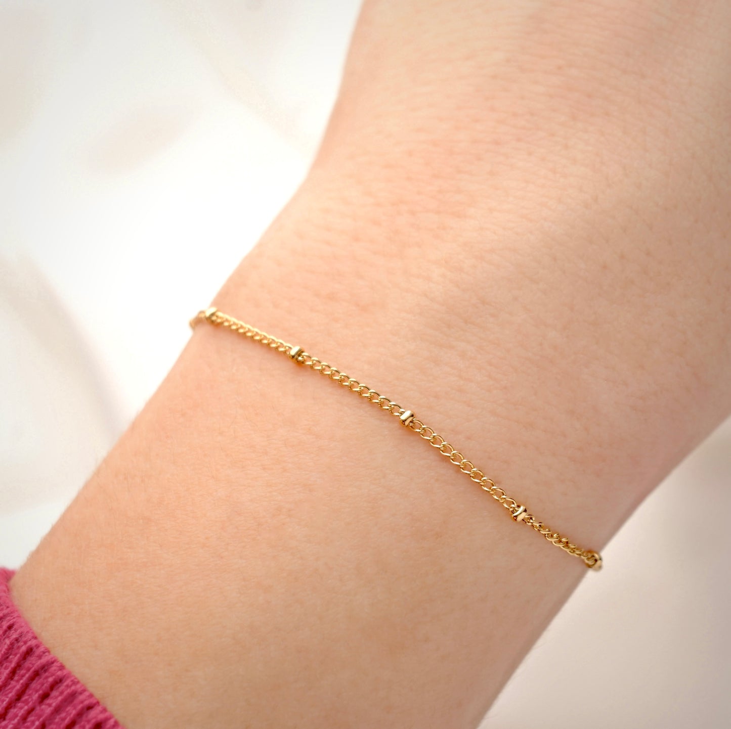 Gold satellite chain on a wrist with a plain background