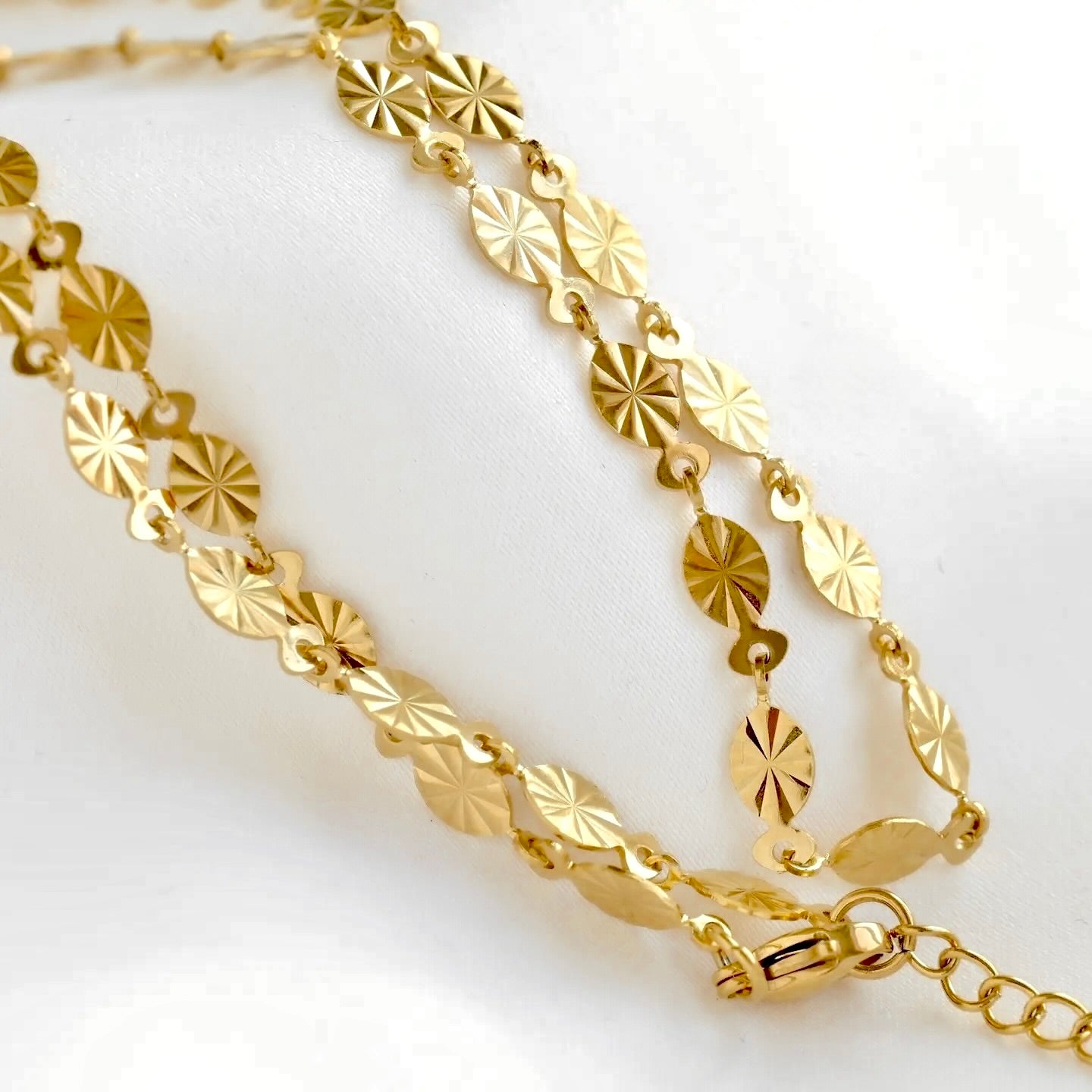 A gold-toned link chain necklace featuring textured, starburst-like oval links, displayed on a clean white background.