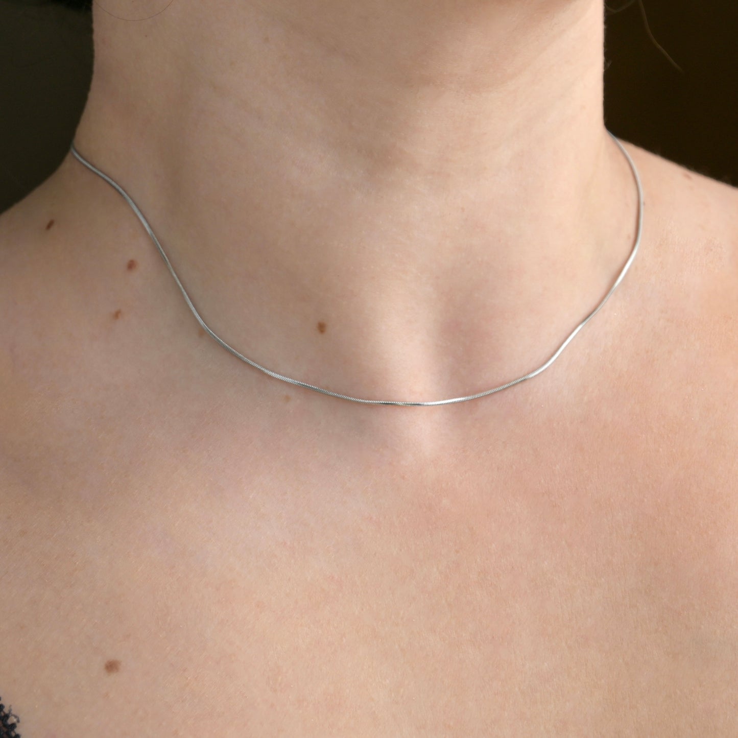 Skinny silver necklace on a person's neck with a plain background