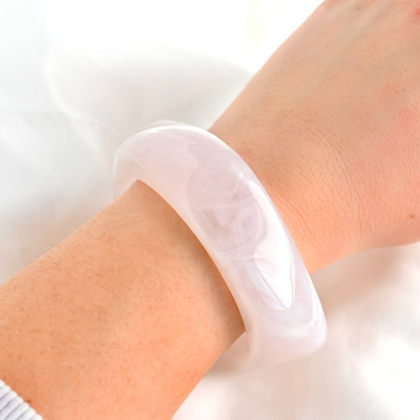 A translucent white resin bangle bracelet worn on a person's wrist, shown against a soft white fabric background.