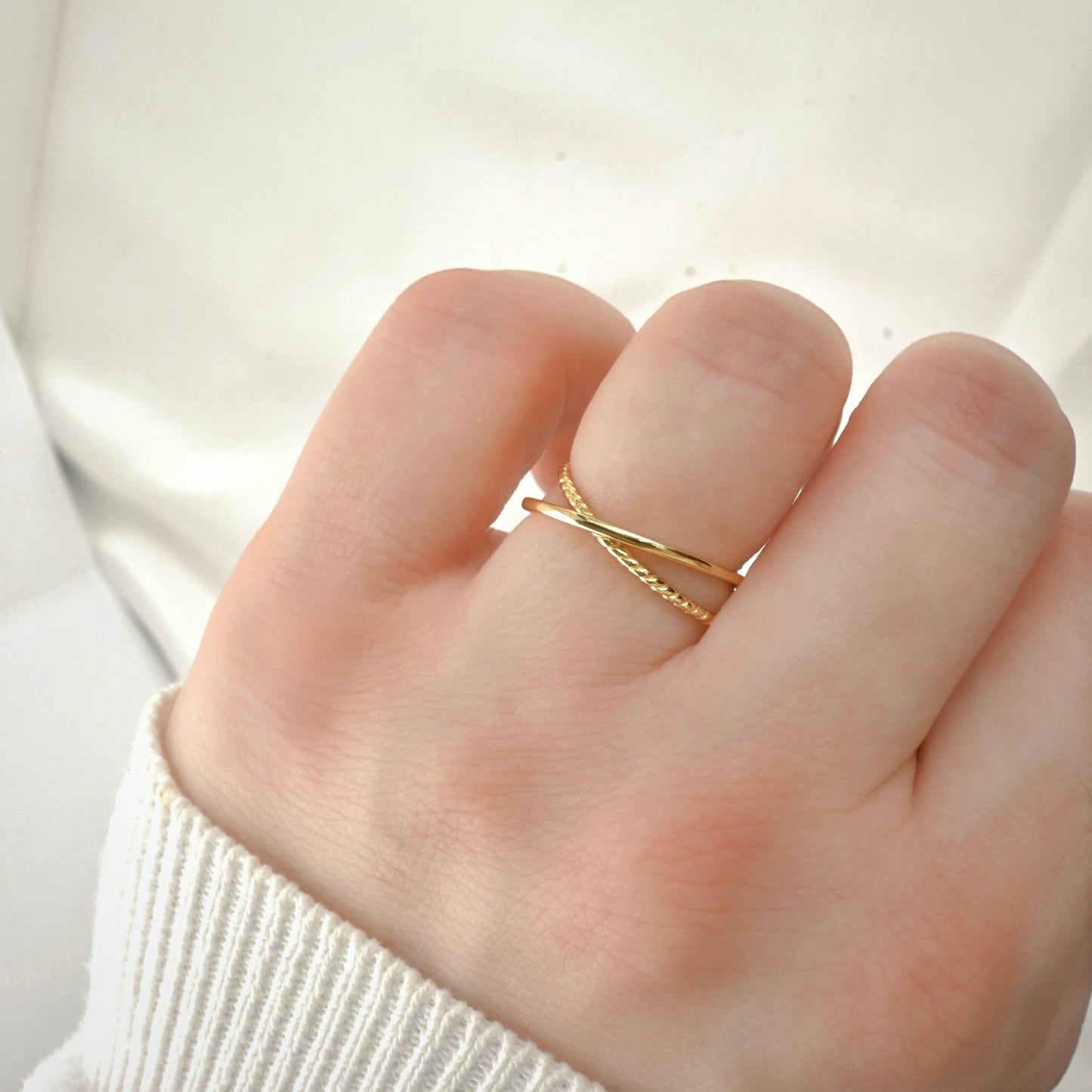 Gold criss cross ring on a finger with two sliminterlocking twisted and smooth bands against a blurred background