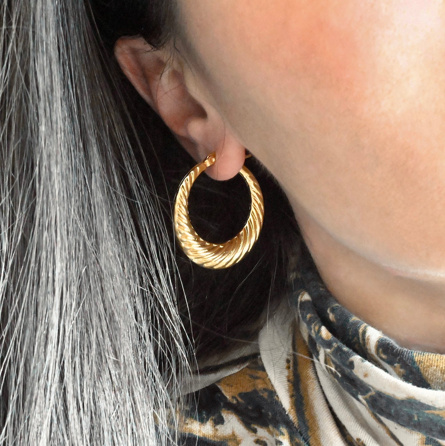 Medium sized twisted gold hoop earrings worn by a person with patterned garment