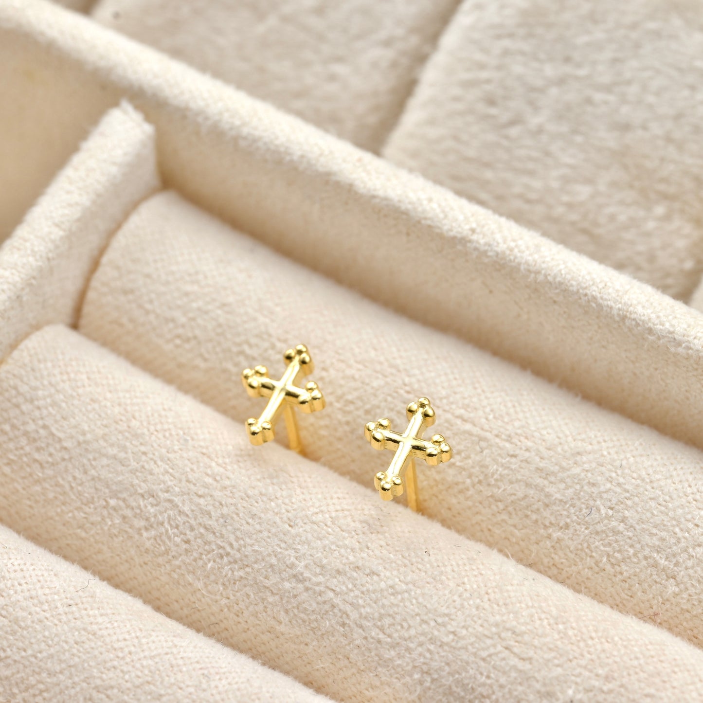 Tiny Gold cross earrings on a textured beige surface