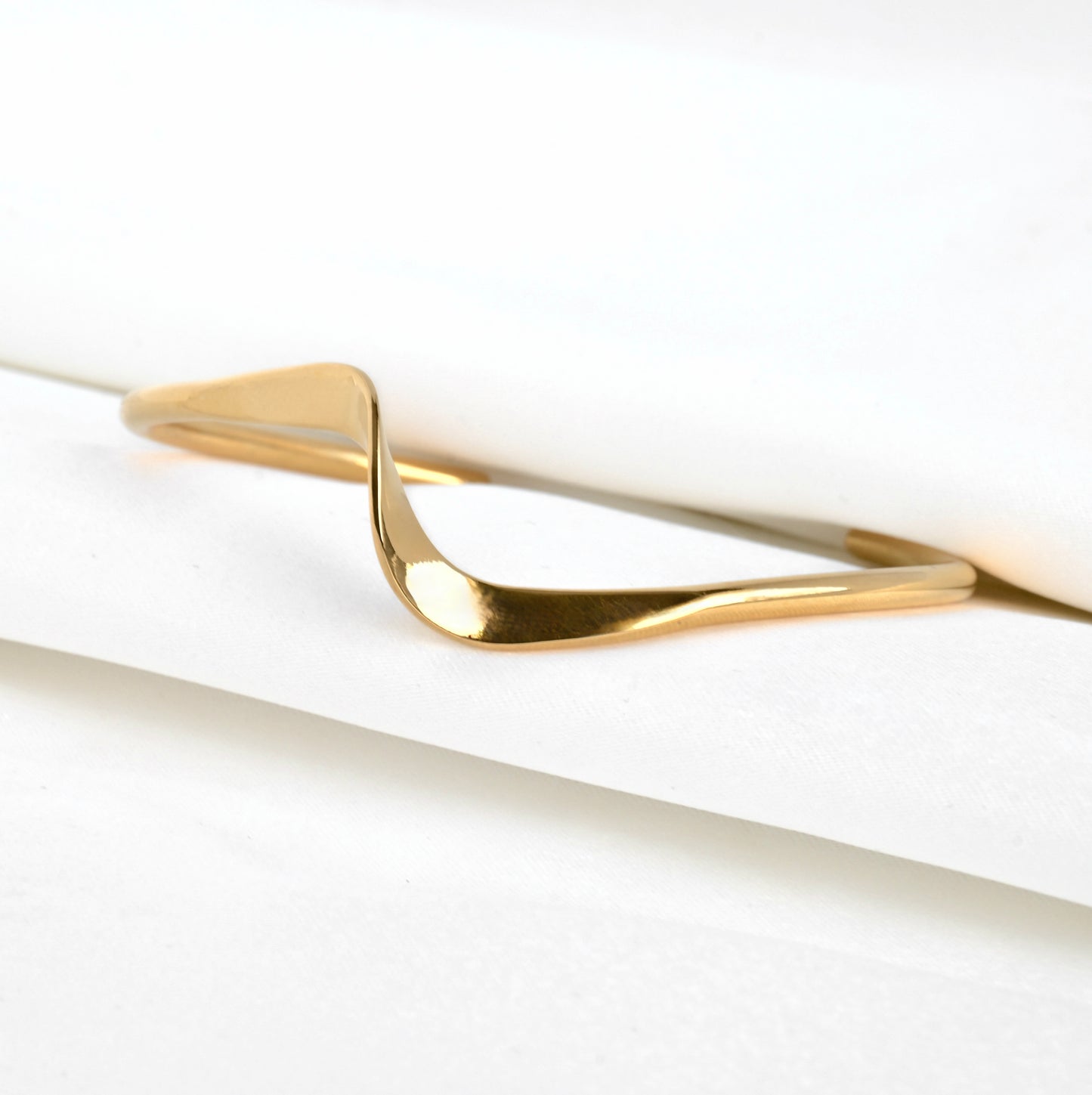 Gold wavy cuff bangle between folded white satin fabric