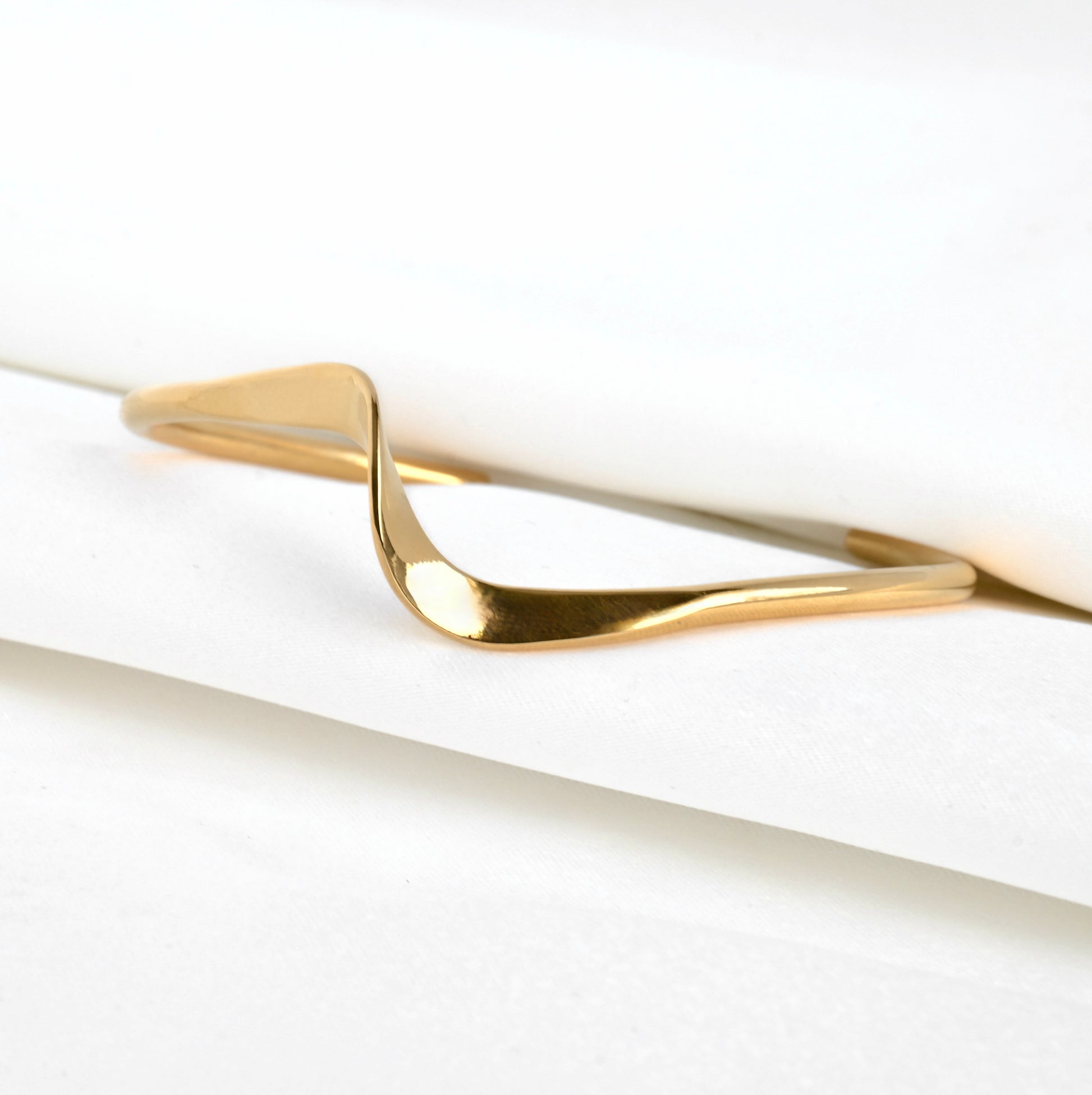 Gold wavy cuff bangle between folded white satin fabric