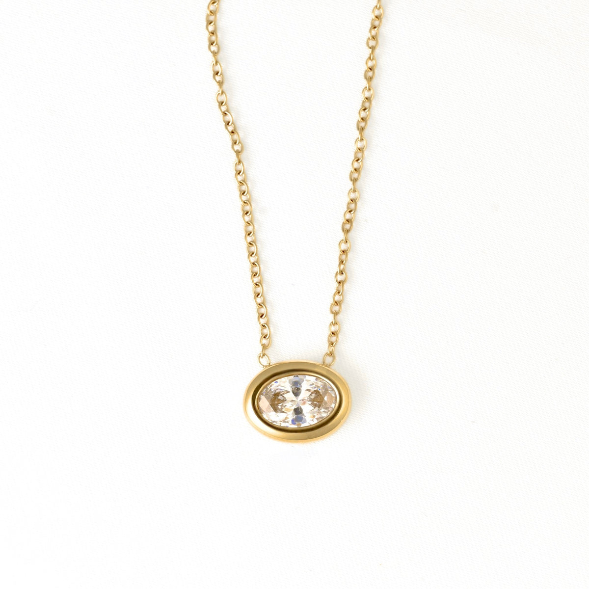 A delicate gold chain necklace with an oval bezel setting holding a clear, faceted gemstone, shown against a plain white background.