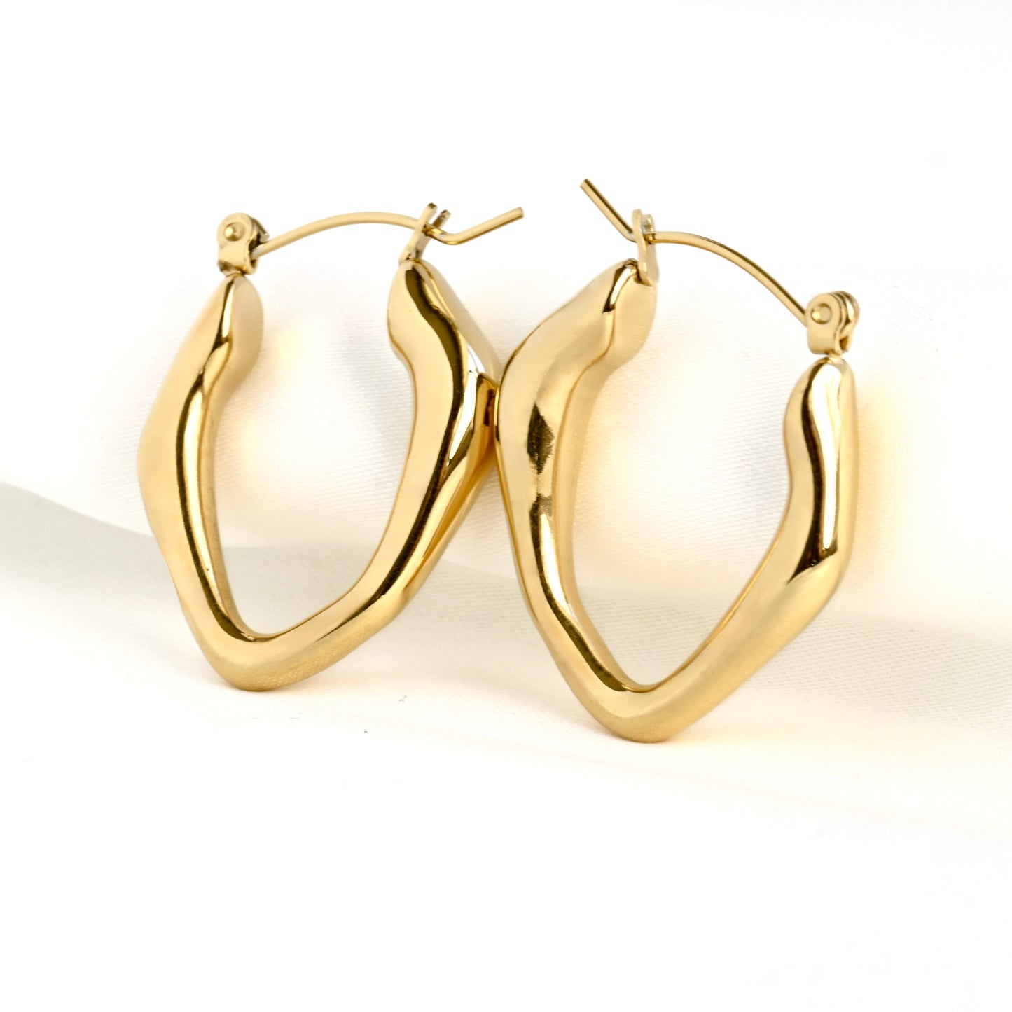 Pair of irregular shape gold hoop earrings on a white background