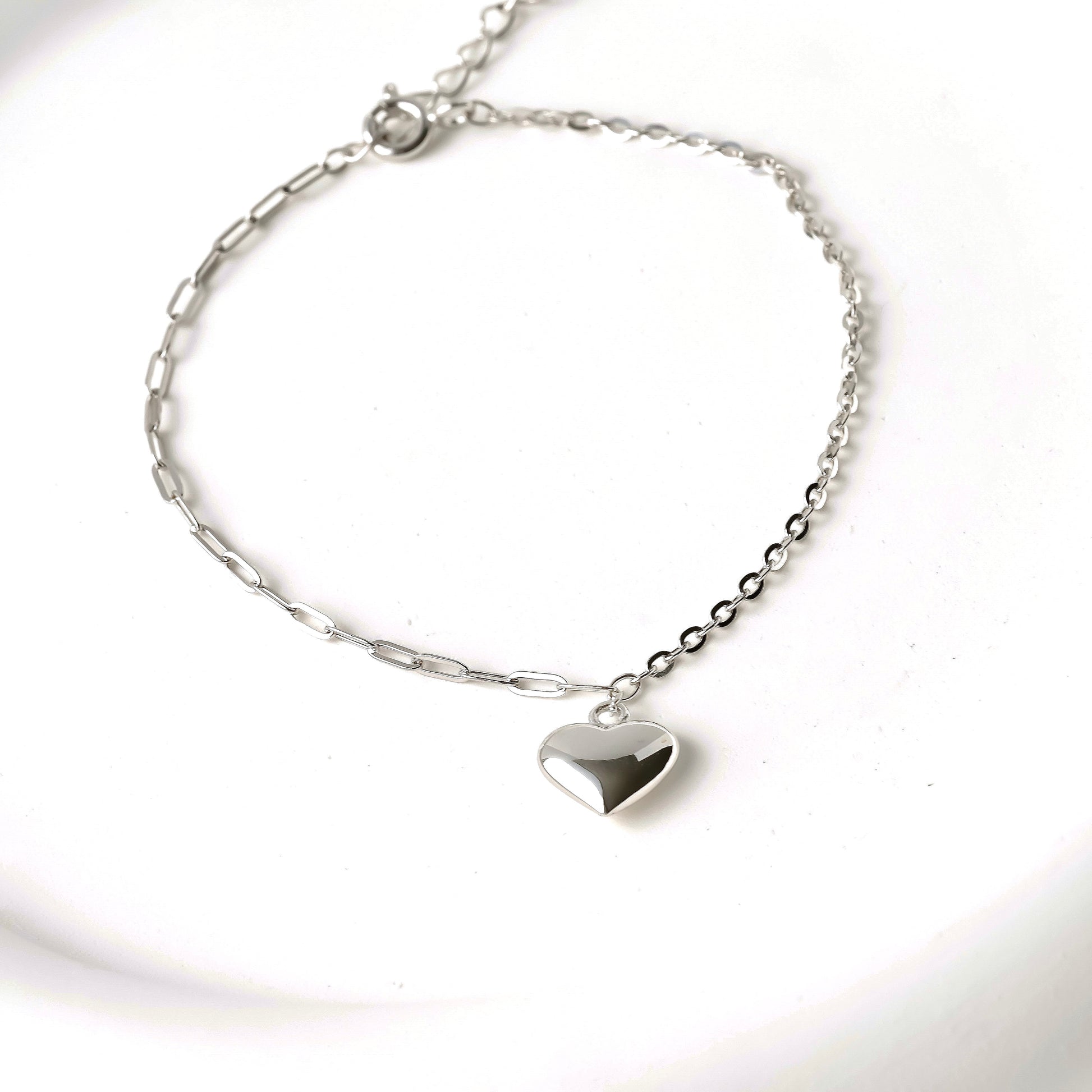 Silver heart pendant bracelet on a mized paperclip and cable chain against a white background