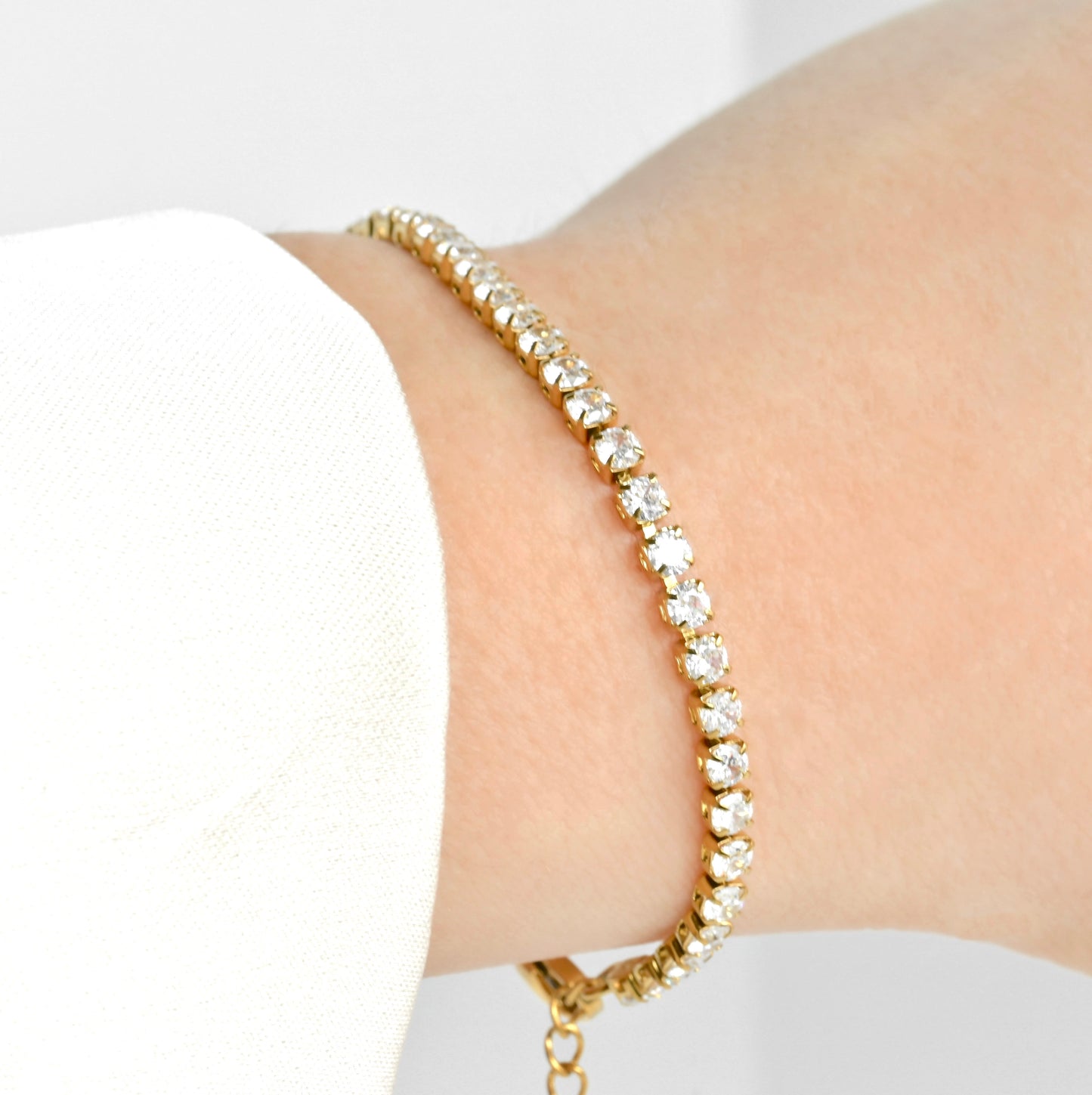 Gold CZ bracelet with clear stones on a wrist against a white background
