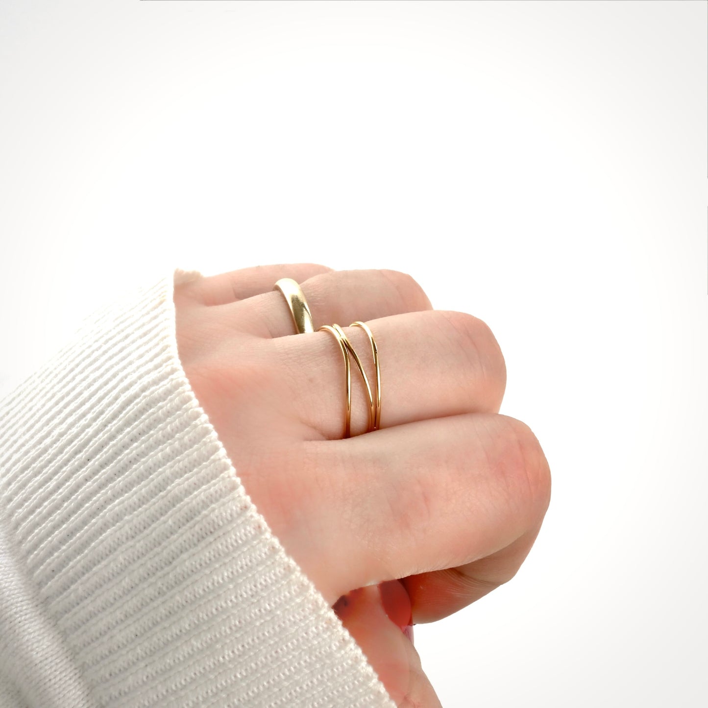 Side view of hand wearing two gold rings on a white background