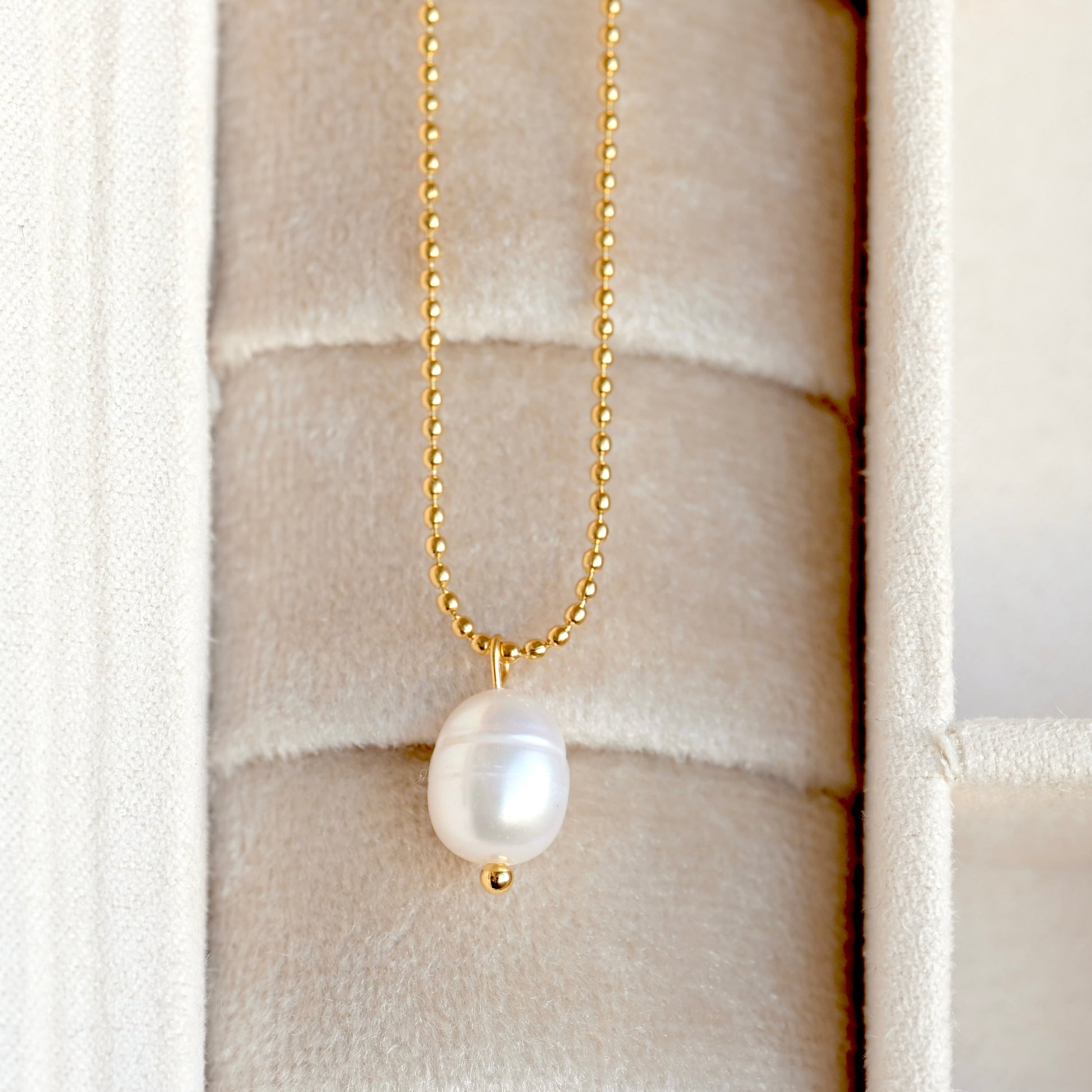 Pearl necklace with gold chain on a textured beige jewelry box