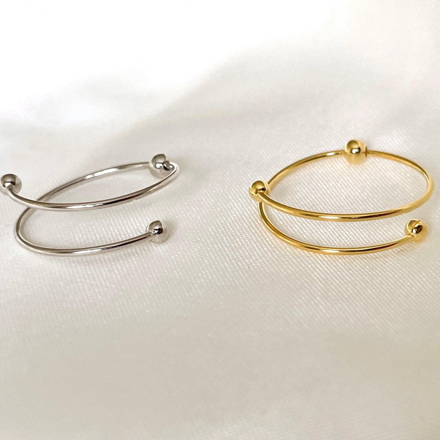 Close up view of two gold and silver wrap rings on a white fabric background