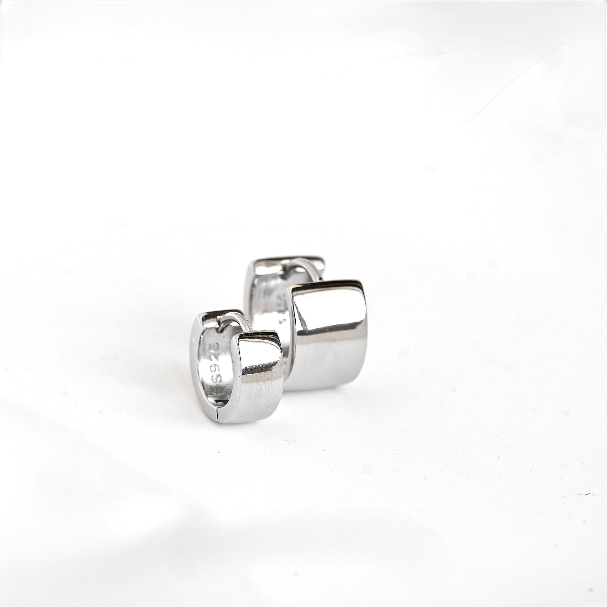 Front view of a pair of polished silver huggie hoop earrings with a rounded rectangular block design, one big and one smaller, displayed on a clean white background.