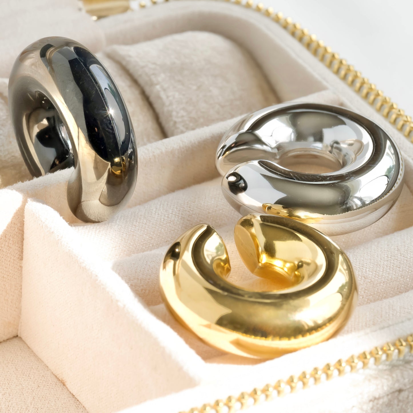 Three metallic rings in a jewelry box with gold, silver, and black colors under direct sunlight