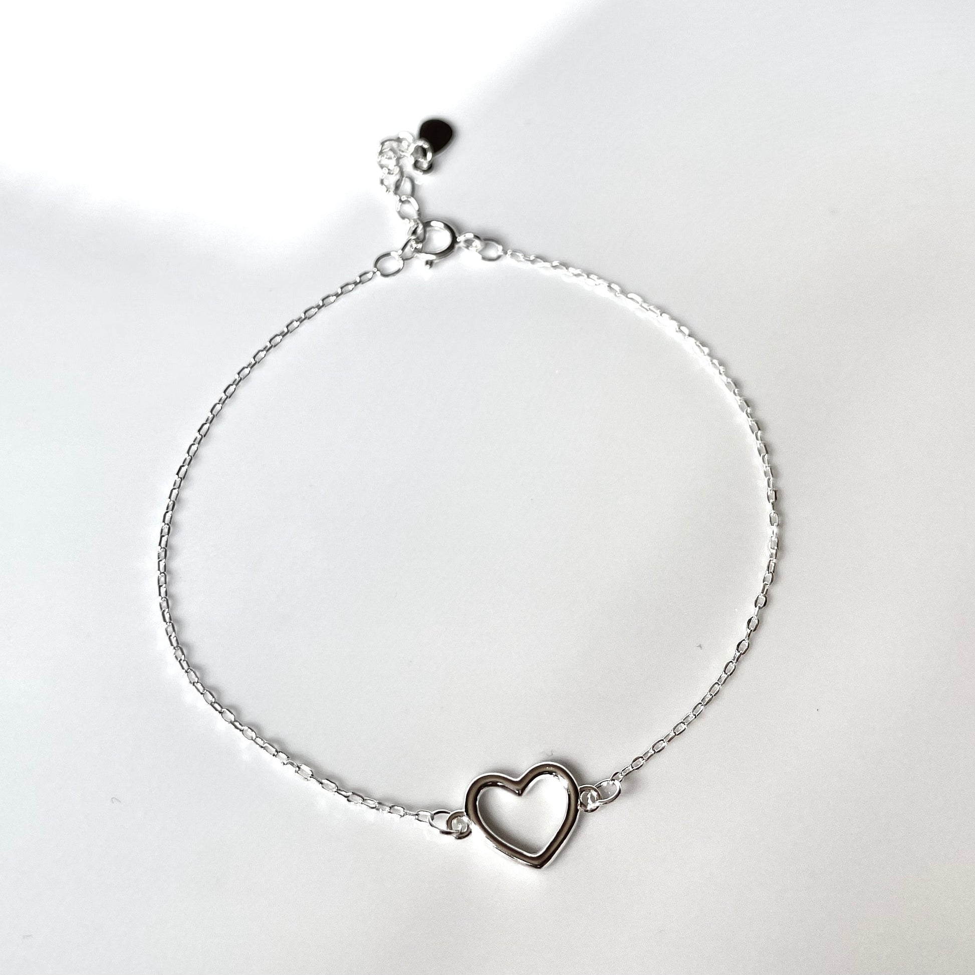 Silver bracelet with a heart charm and a ultra fine cable chain on a white background