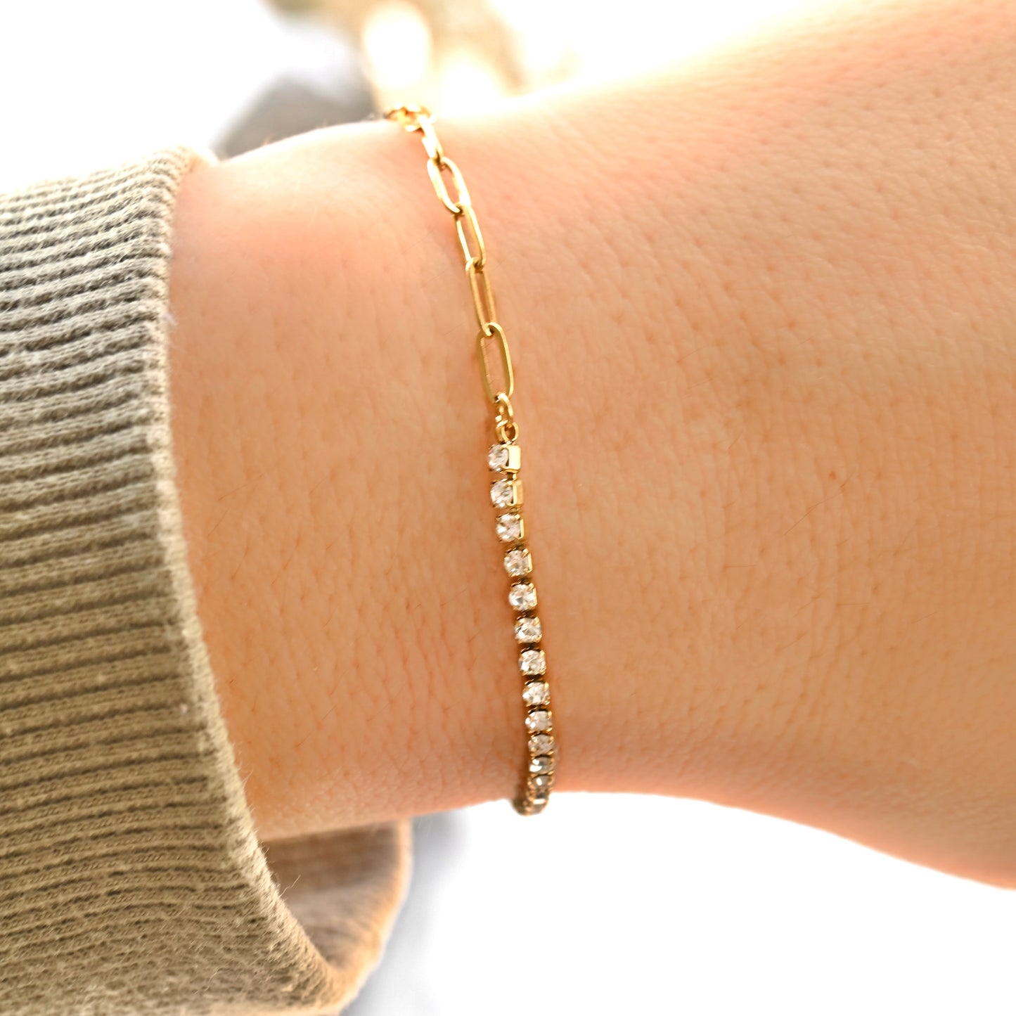 Gold paperclip and tennis bracelet with small diamonds on a wrist against a neutral background