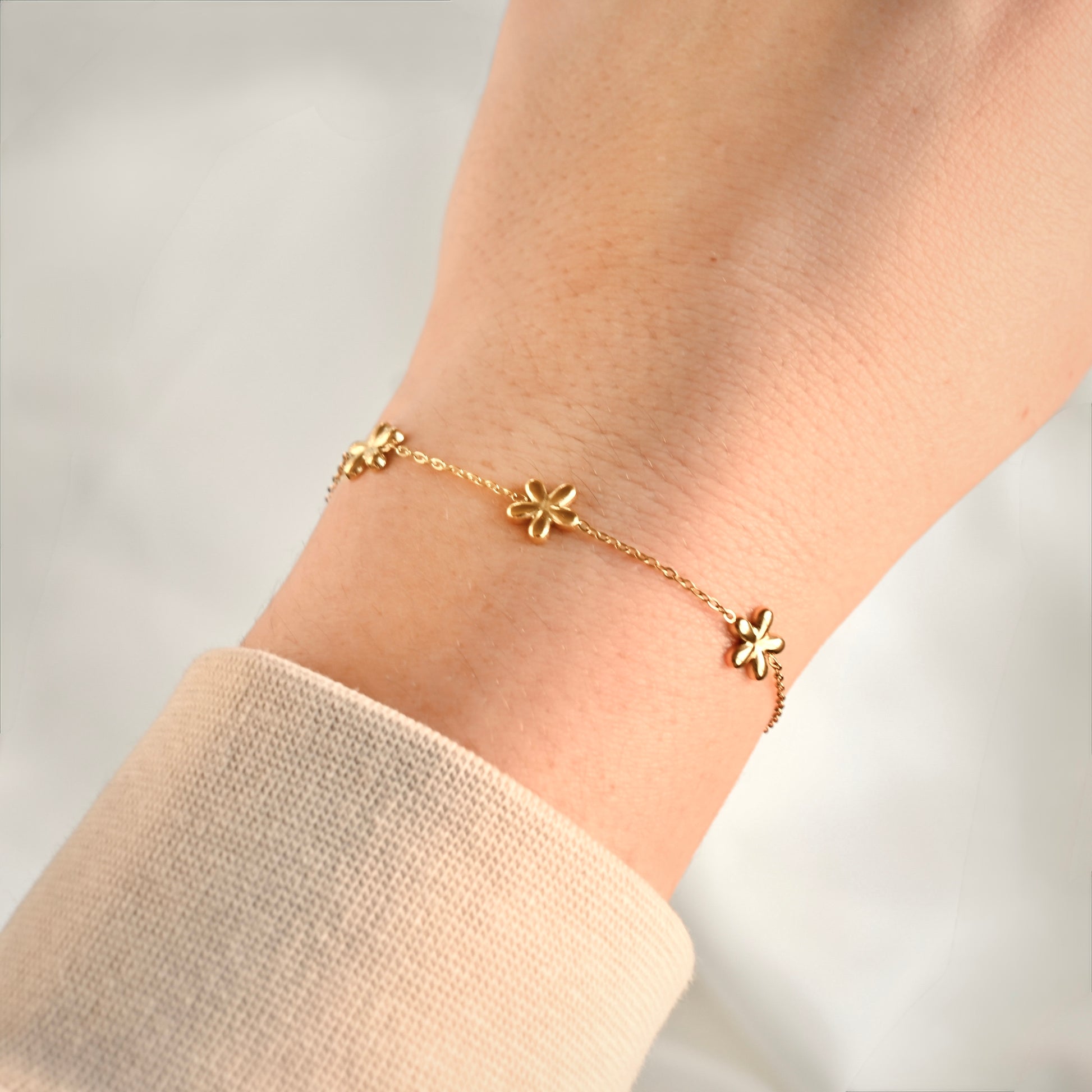 Gold bracelet with daisy-shaped charms on a person's wrist against a neutral background