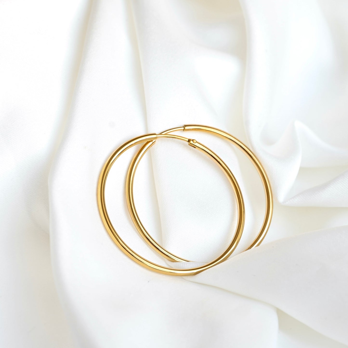A pair of thin eternity gold hoops resting on draped white fabric.