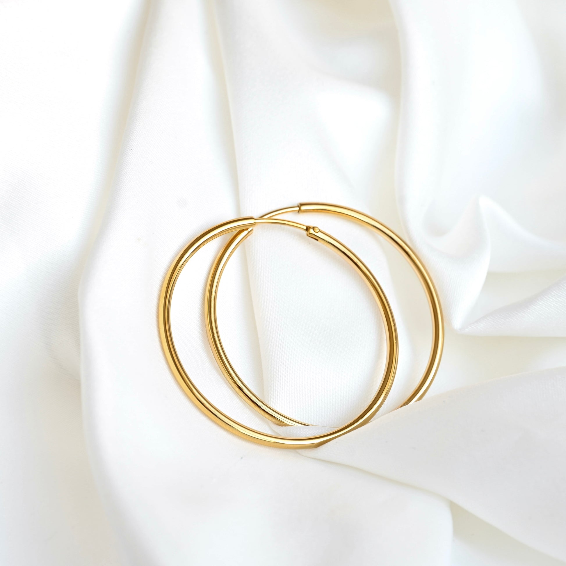 A pair of thin eternity gold hoops resting on draped white fabric.