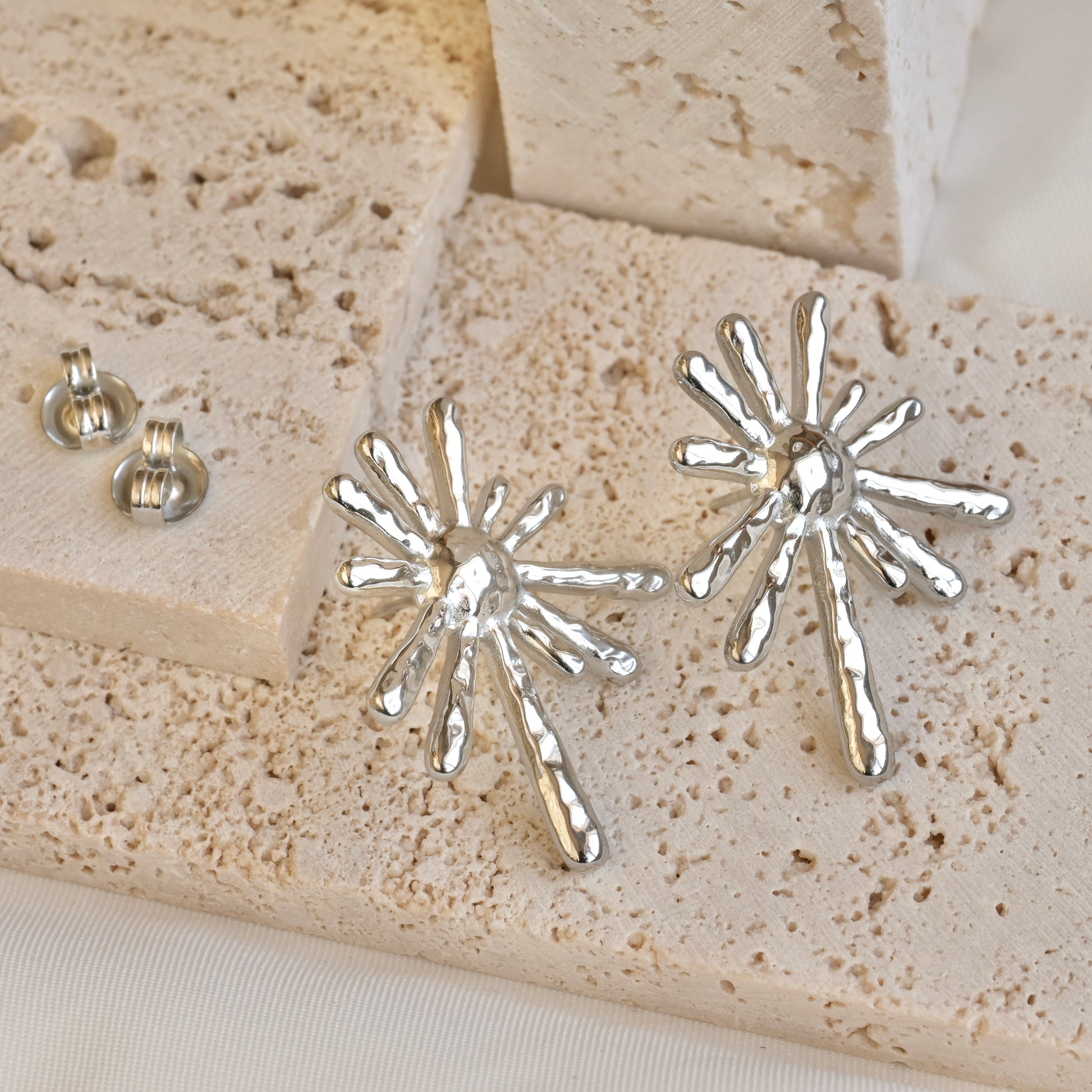 Silver starburst earrings on a textured stone surface
