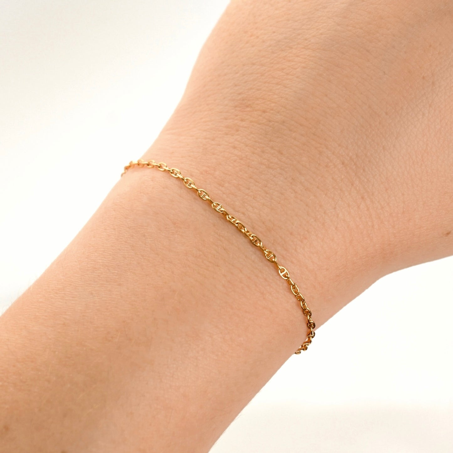 A delicate gold chain bracelet worn on a person's wrist, shown against a clean white background.