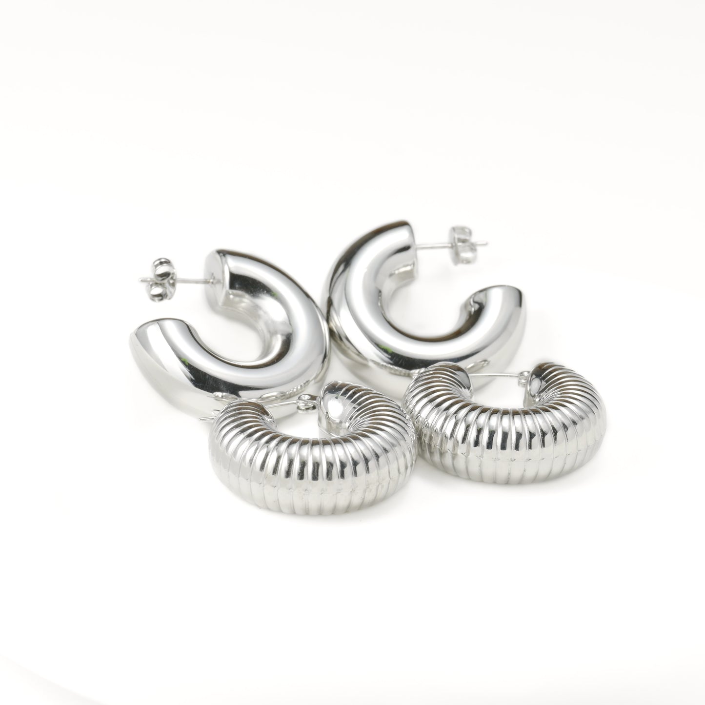 Set of thick silver hoop earrings with plain and textured designs on a white background